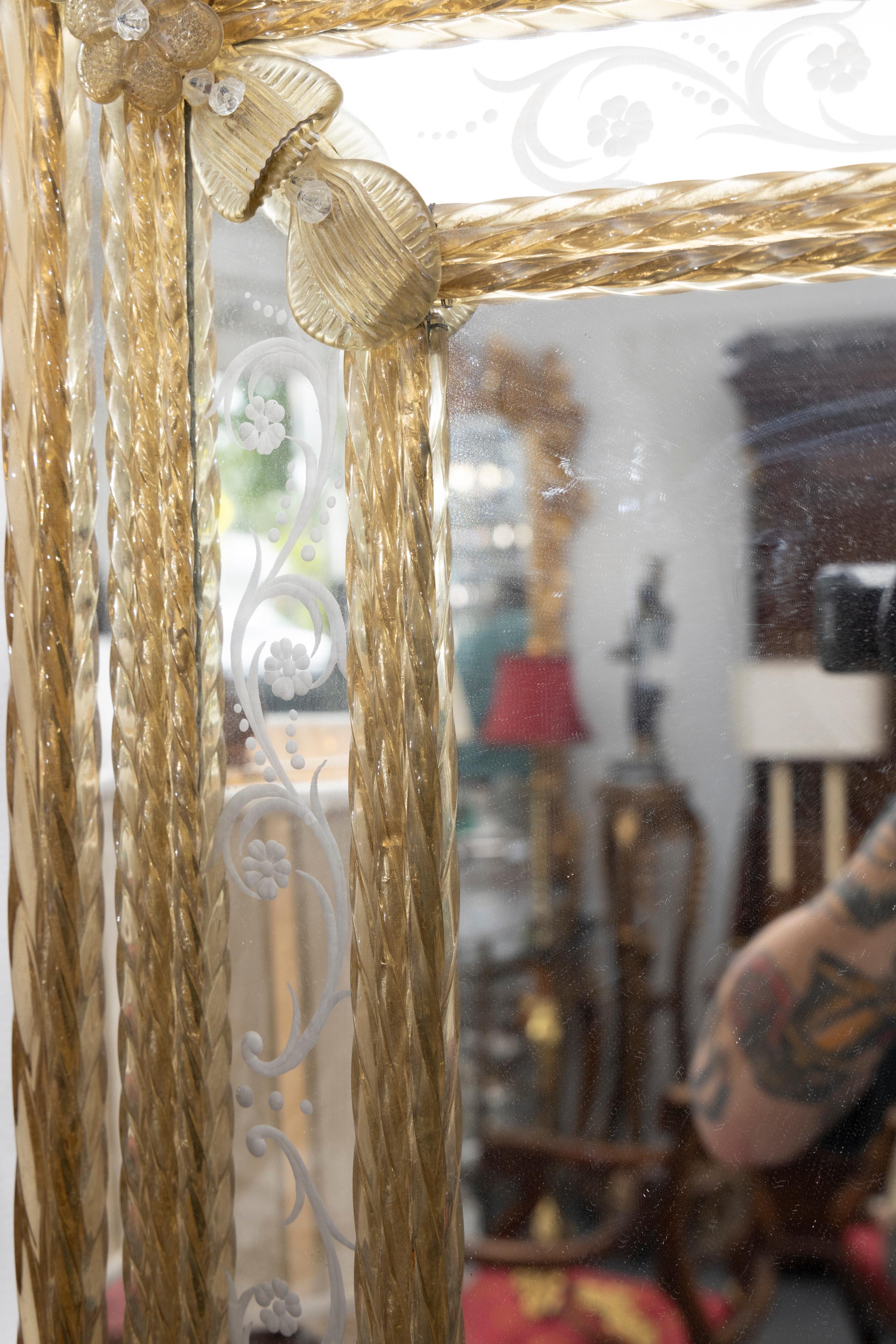 Il s'agit d'un joli miroir vénitien italien romantique dont la plaque de verre est encadrée par un cadre en verre gravé et une corniche encadrée par des tiges torsadées en verre ambré et ponctuée par des têtes de fleurs en verre ambré.