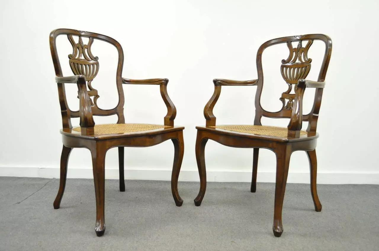 Stunning pair of vintage solid cherry wood, distress finished, hand-carved armchairs in the Rococo taste. The pair features shapely carved urn form backsplats, cane seats, cabriole legs, and a desirable and original antiqued finish. Made in Italy
