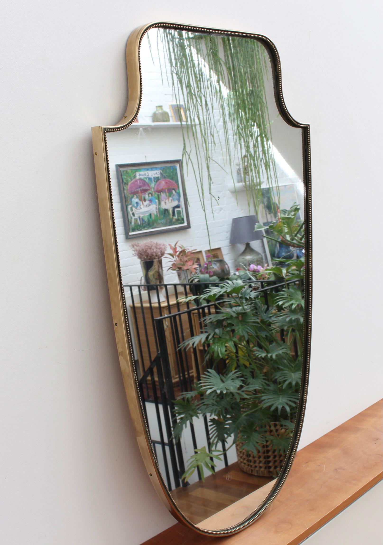 Mid-Century Italian wall mirror with brass frame and beading (circa 1950s). This mirror is simply elegant and characterful in a modern, Gio Ponti style. It is large, classically crest-shaped with a delightful beading adding visual interest. It is