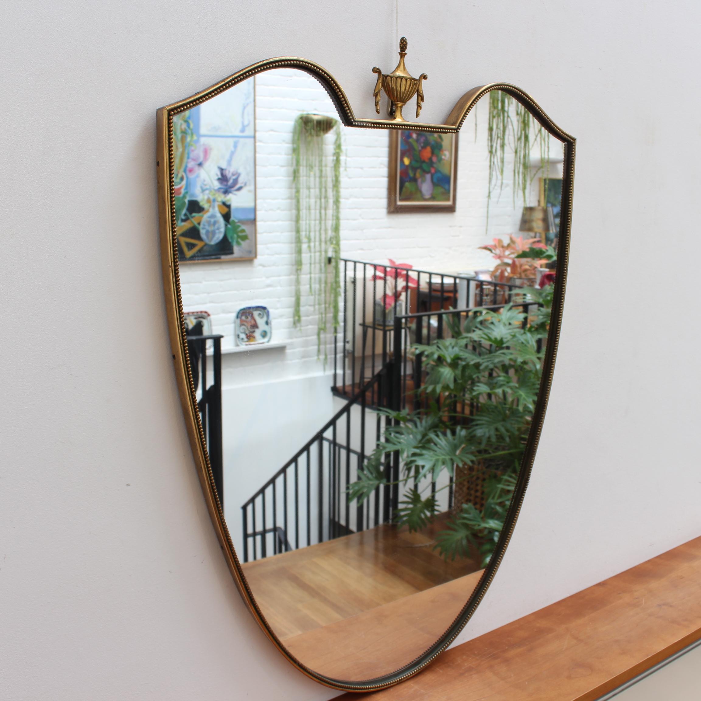 Vintage Italian wall mirror with brass frame with beading and decorative crowning (circa 1950s). The mirror is a crest shape with a rare crowning feature which delights the viewer as an unexpected surprise. Always classically elegant in a modern Gio