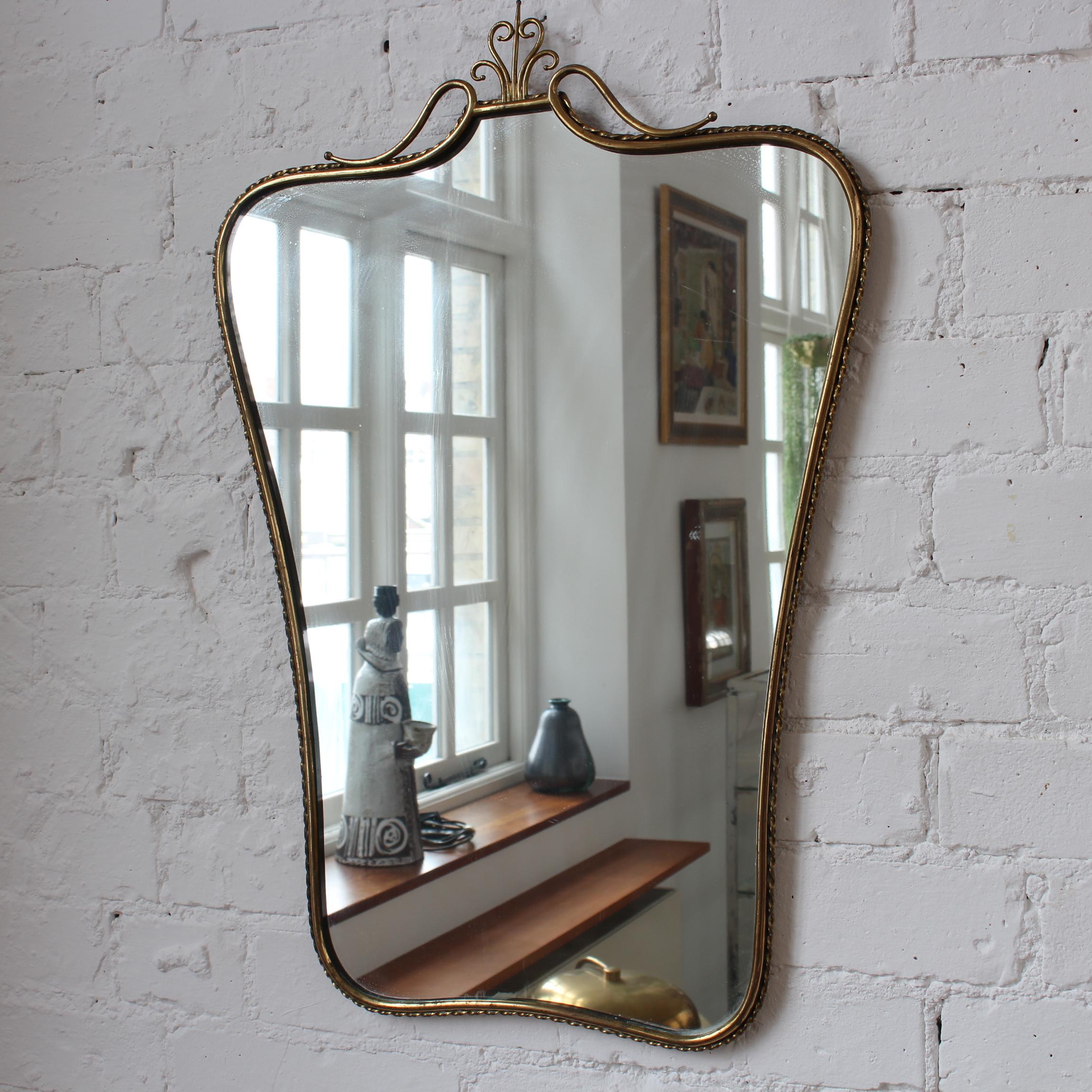 Mid-Century Italian wall mirror with brass frame and top flourish (circa 1960s). This mirror is simply elegant and characterful in a modern, Gio Ponti style. It is classically-shaped presenting a charming top flourish in the form of a decorative