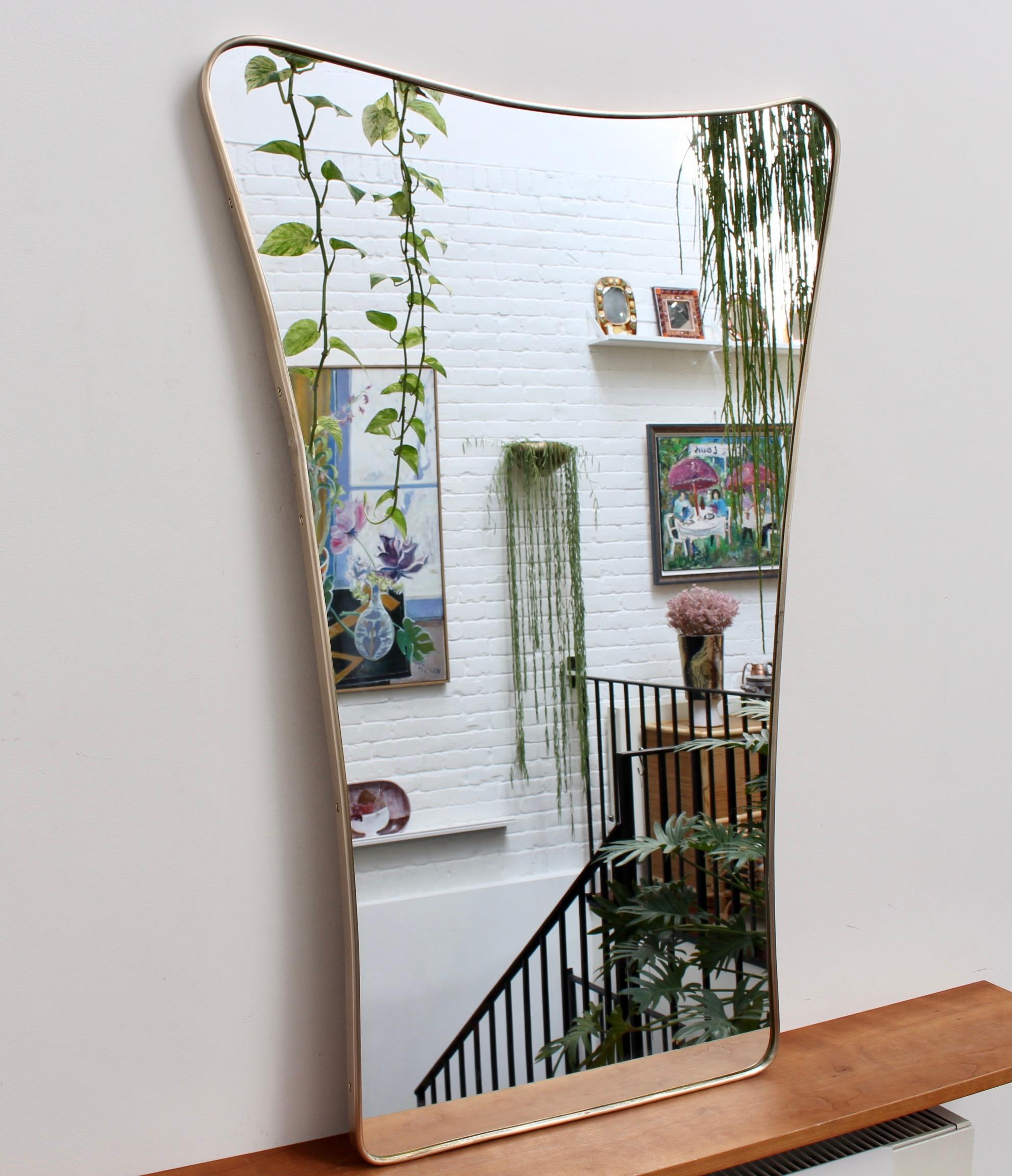 Mid-century Italian wall mirror with brass frame (circa 1950s). A large mirror in the form of a shield, or more whimsically, shaped like a key hole. It is one of the most beautiful shapes encountered from the enormous selection of brass-framed