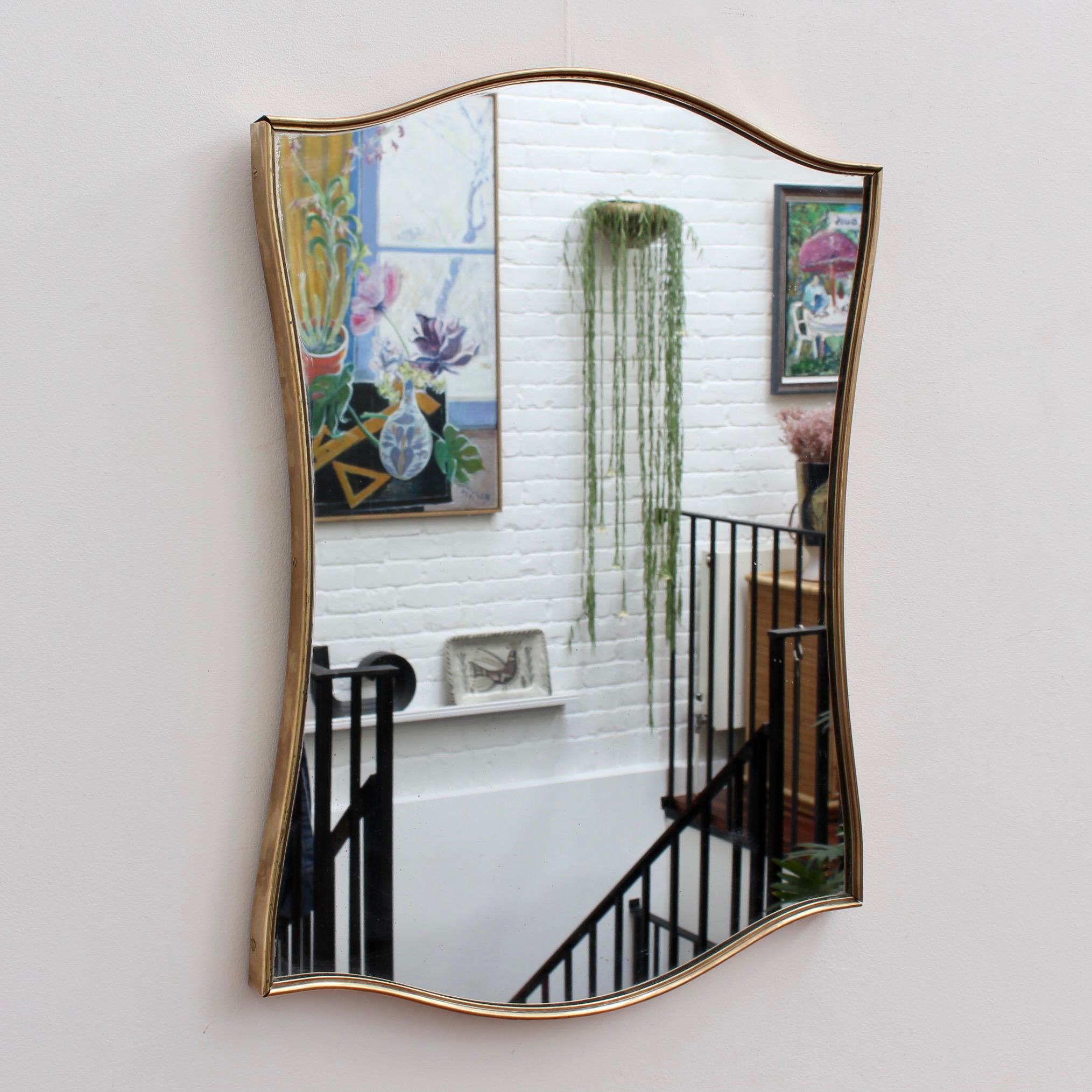 Mid-century Italian wall mirror with brass frame (circa 1950s). This medium-sized mirror is beautifully-shaped and distinctive in a modern Gio Ponti style and is in overall very good condition. There is some very minor blemishing on the lower right