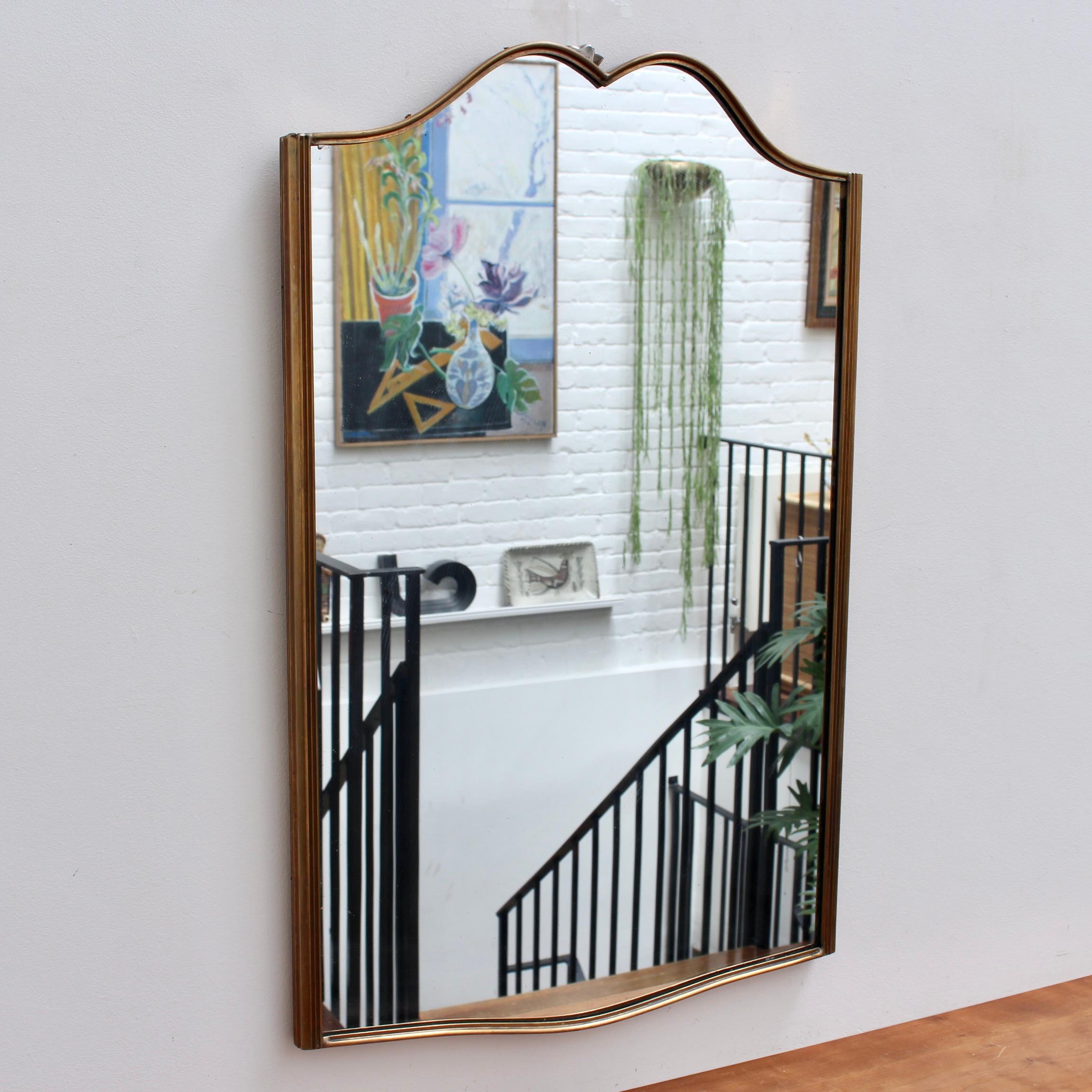 Mid-century Italian wall mirror with brass frame (circa 1950s). The mirror is elegantly shaped with wavy curves which join at the top and a single curve on the lower horizontal of the frame. Always classically distinctive in a modern, Gio Ponti