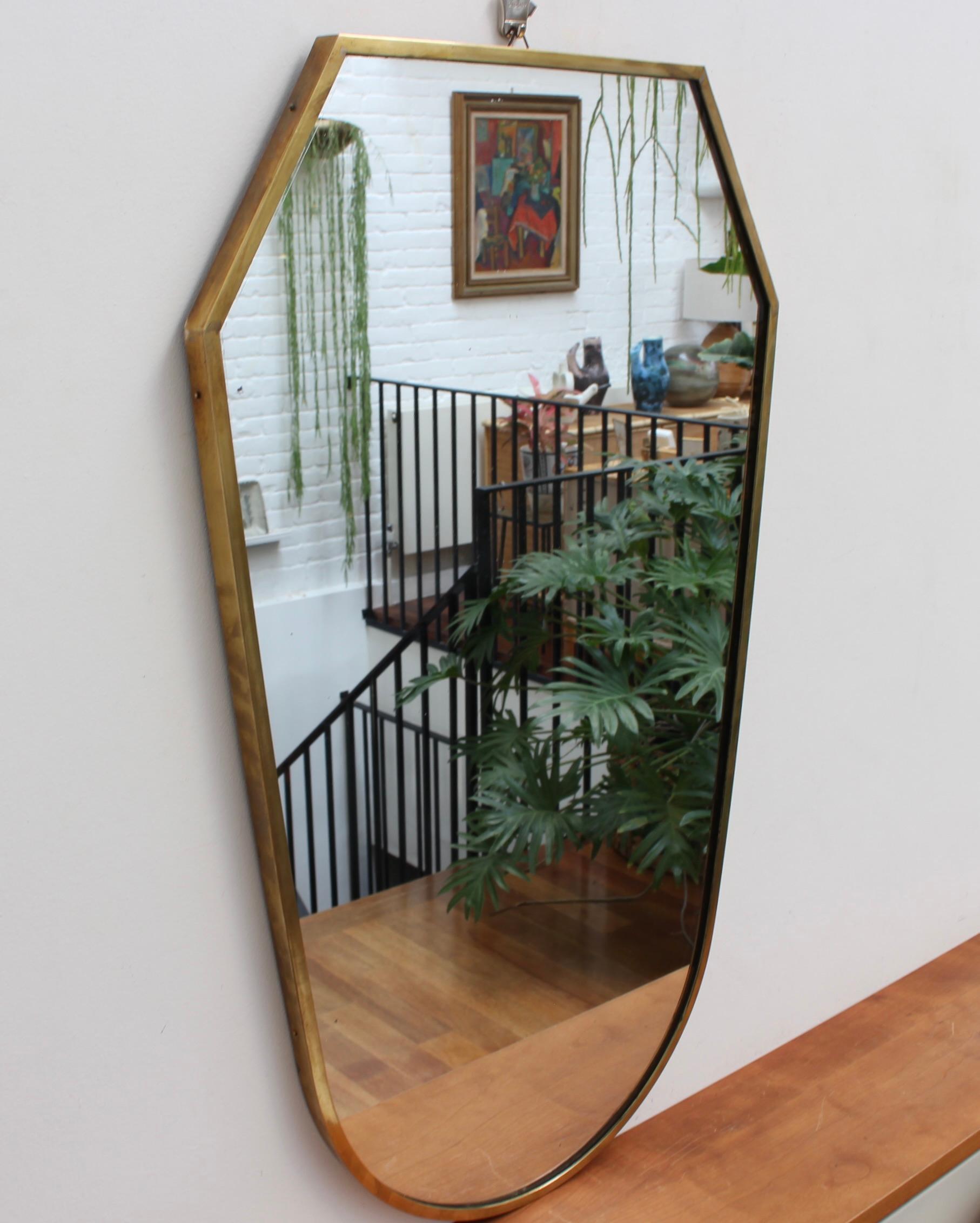 Mid-century Italian wall mirror with brass frame (circa 1950s). This mirror is simply elegant and characterful in a modern style. It is an angular, crest-shaped piece and in good overall condition. A characterful patina covers much of the brass