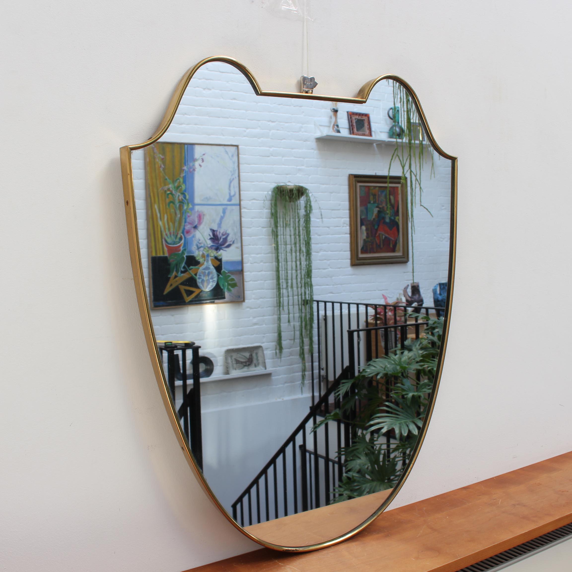 Mid-century Italian wall mirror with brass frame (circa 1950s). The mirror is classically-shaped and distinctive in a Modern style. It is in good overall condition including the glass. The frame presents an age-related patina which simply adds
