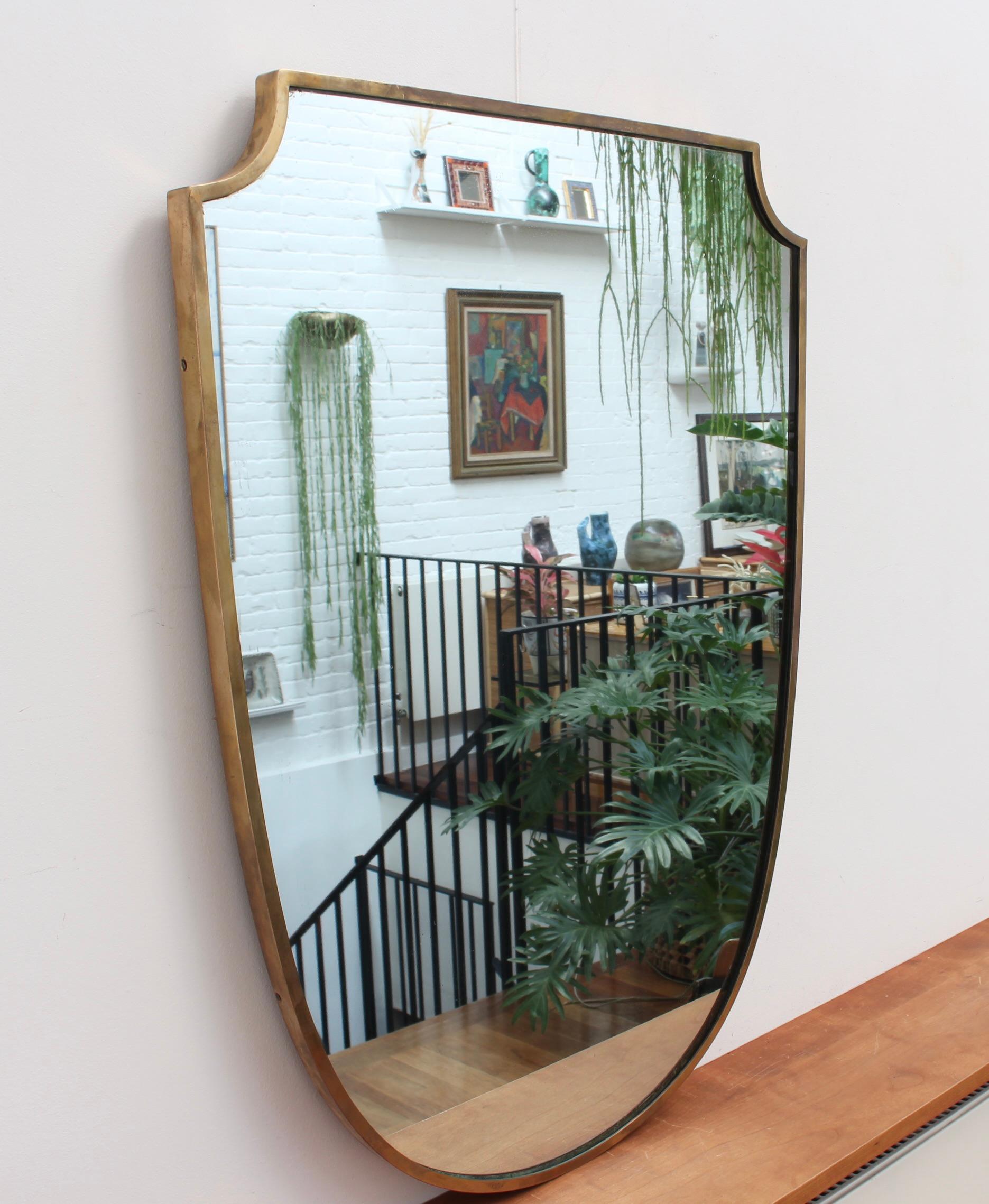 Midcentury Italian wall mirror with brass frame (circa 1950s). The mirror is classically-shaped and distinctive in a Gio Ponti style. The frame is in good overall condition with a characterful, age-related patina. The mirror glass is in fair