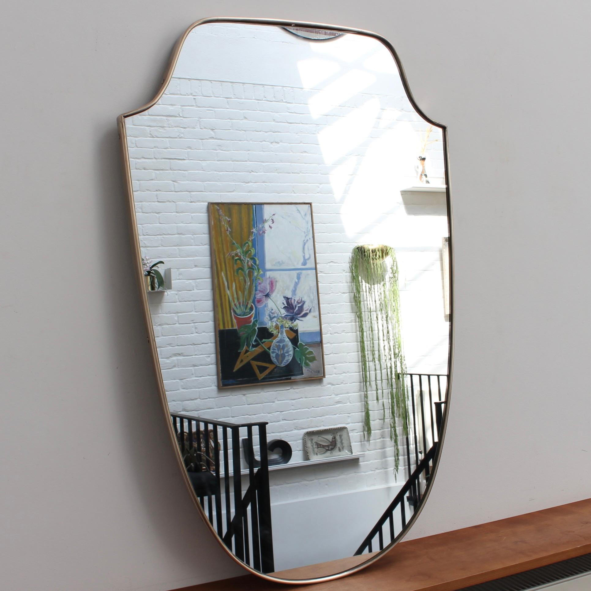 Midcentury Italian wall mirror with brass frame (circa 1950s). The large mirror is classically-shaped and distinctive in a Modern style. It is in good overall condition with a minor chip in the upper right of the mirror - see photos. A beautiful,