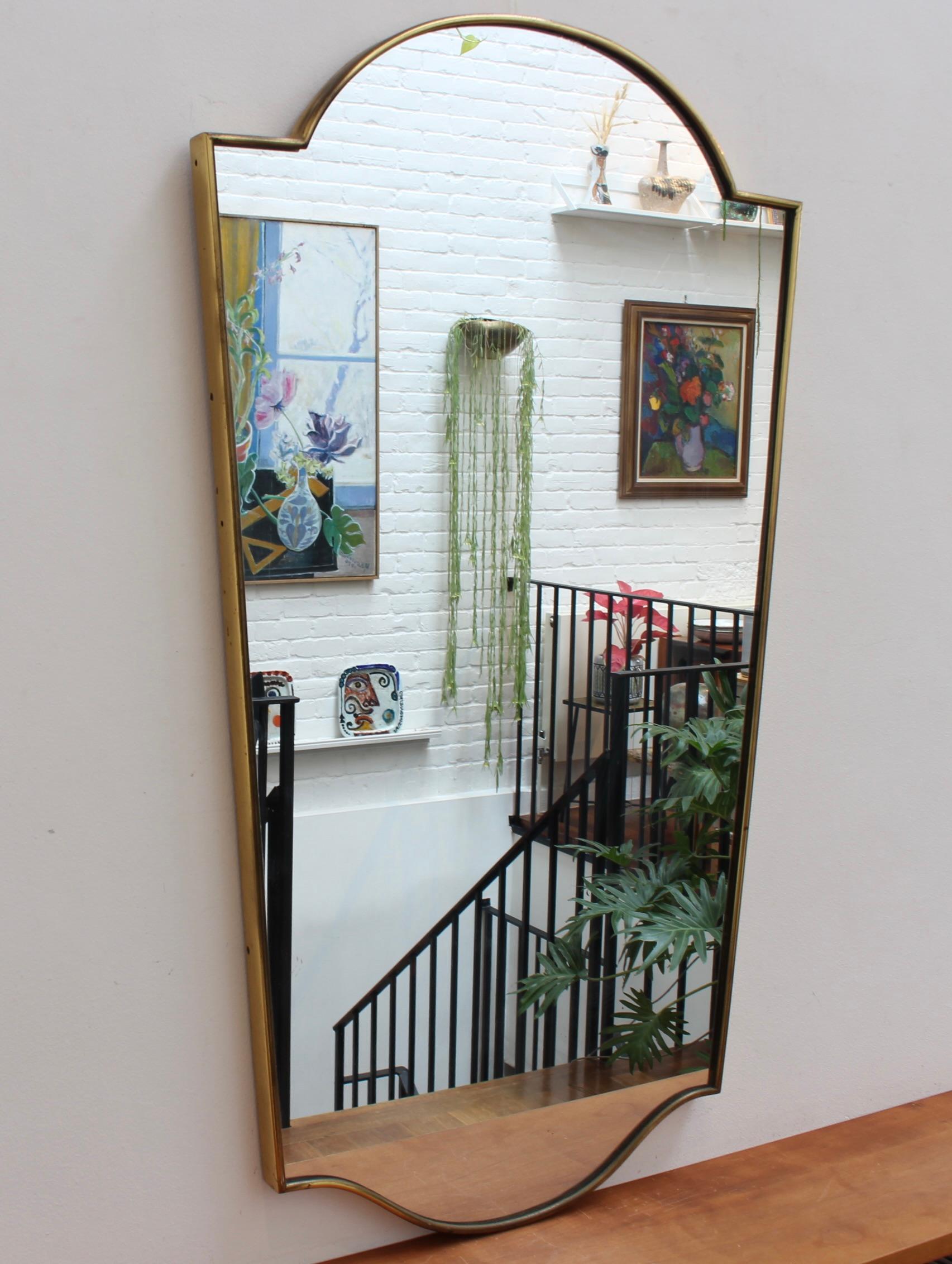 Mid-century Italian wall mirror with brass frame (circa 1950s). The mirror is classically-shaped and distinctive in a Modern style. It is in good overall condition considering the presence of a small malformation in the glass near the top (see
