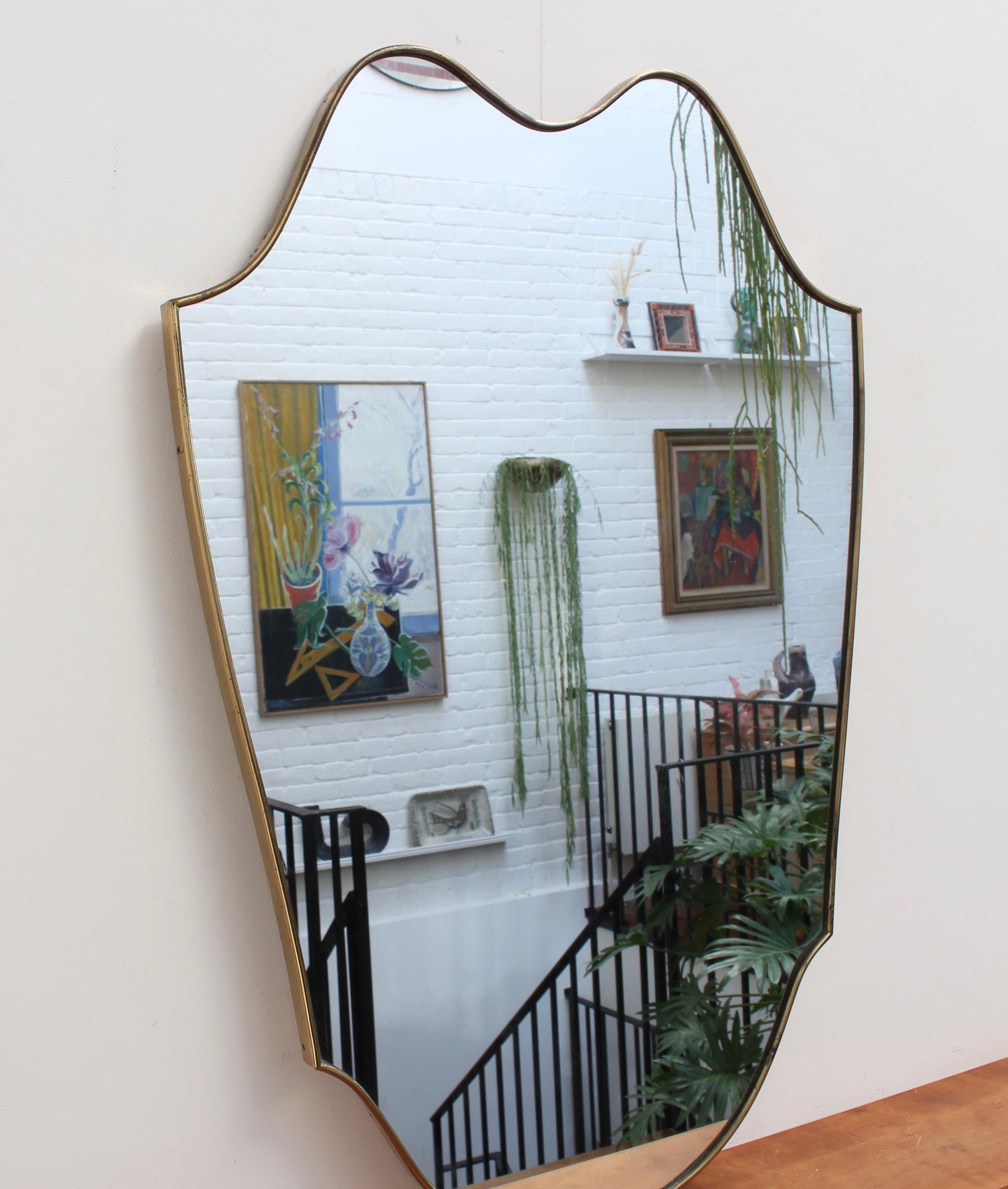 Large mid-century Italian wall mirror with brass frame (circa 1950s). The mirror is classically-shaped and distinctive in a Modern style. The glass is in good condition - the frame has an aged, characterful patina and is in fair condition. It is