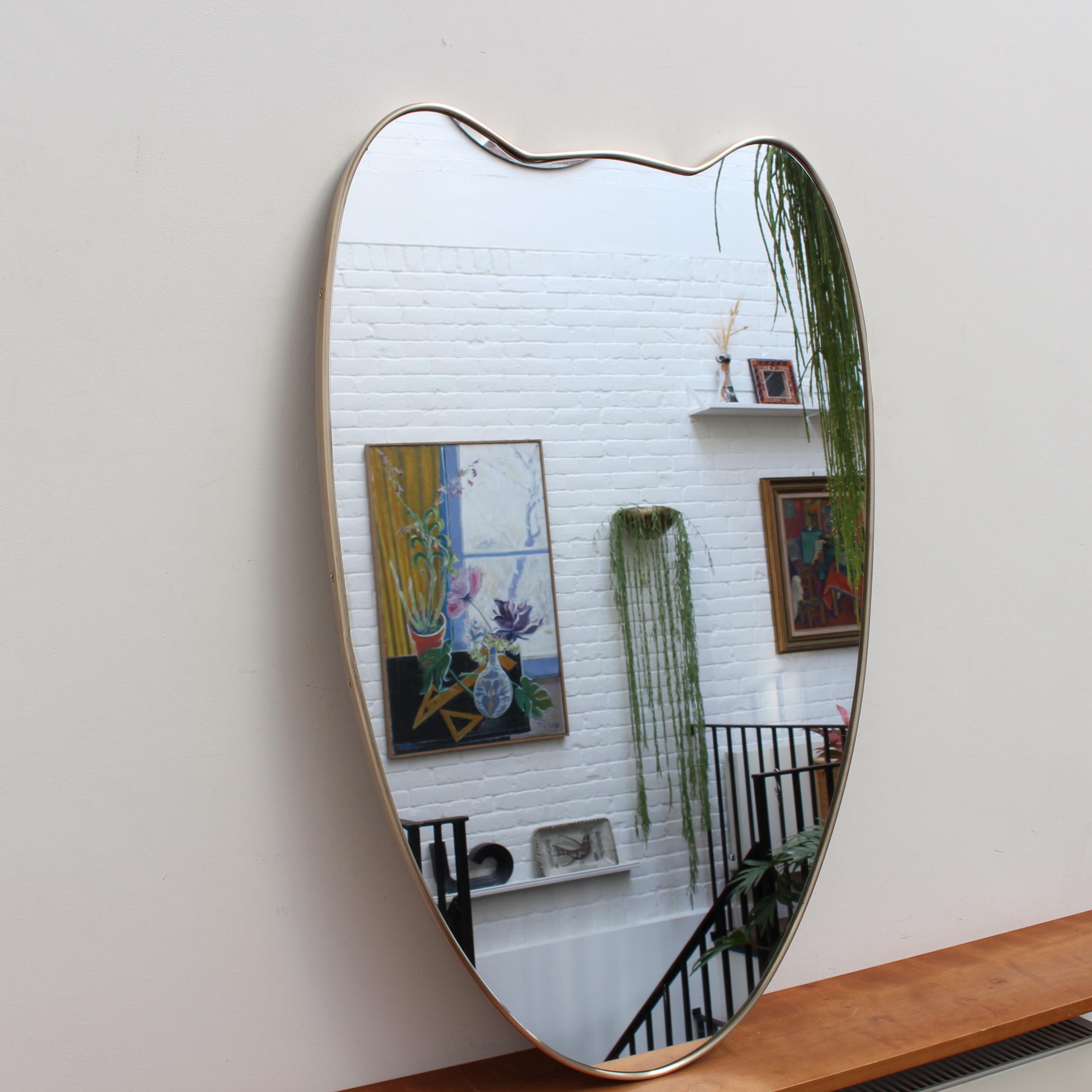Miroir mural italien du milieu du siècle avec cadre en laiton (circa 1950s). Le miroir a une forme classique et distinctive dans un style moderne. Il est en très bon état général. Une belle patine vieillie se développera au fil du temps sur le cadre