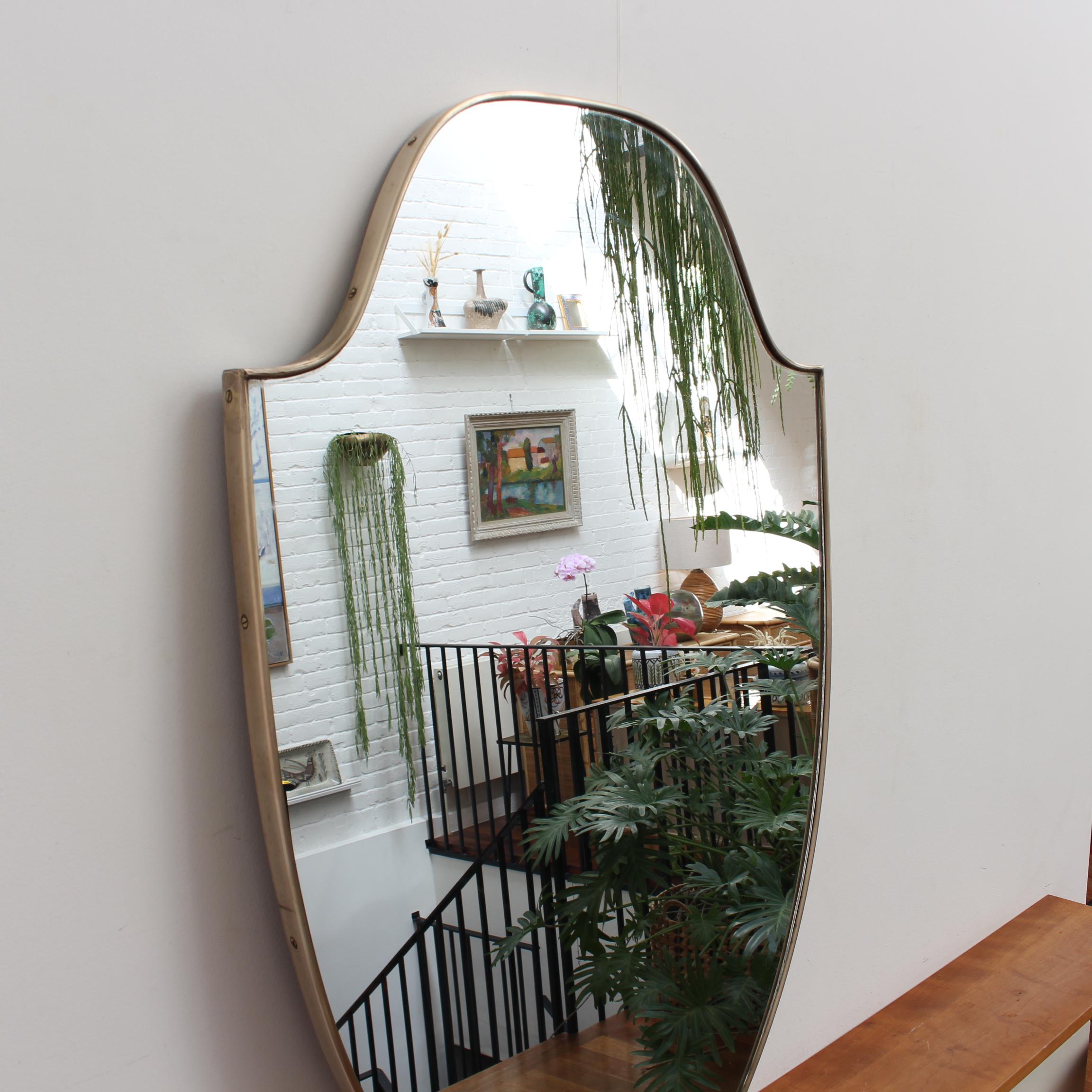 Midcentury Italian wall mirror with brass frame (circa 1950s). The mirror is classically-shaped and distinctive in a Modern style. It is in very good overall condition. A beautiful patina develops on the brass frame - this one has been recently