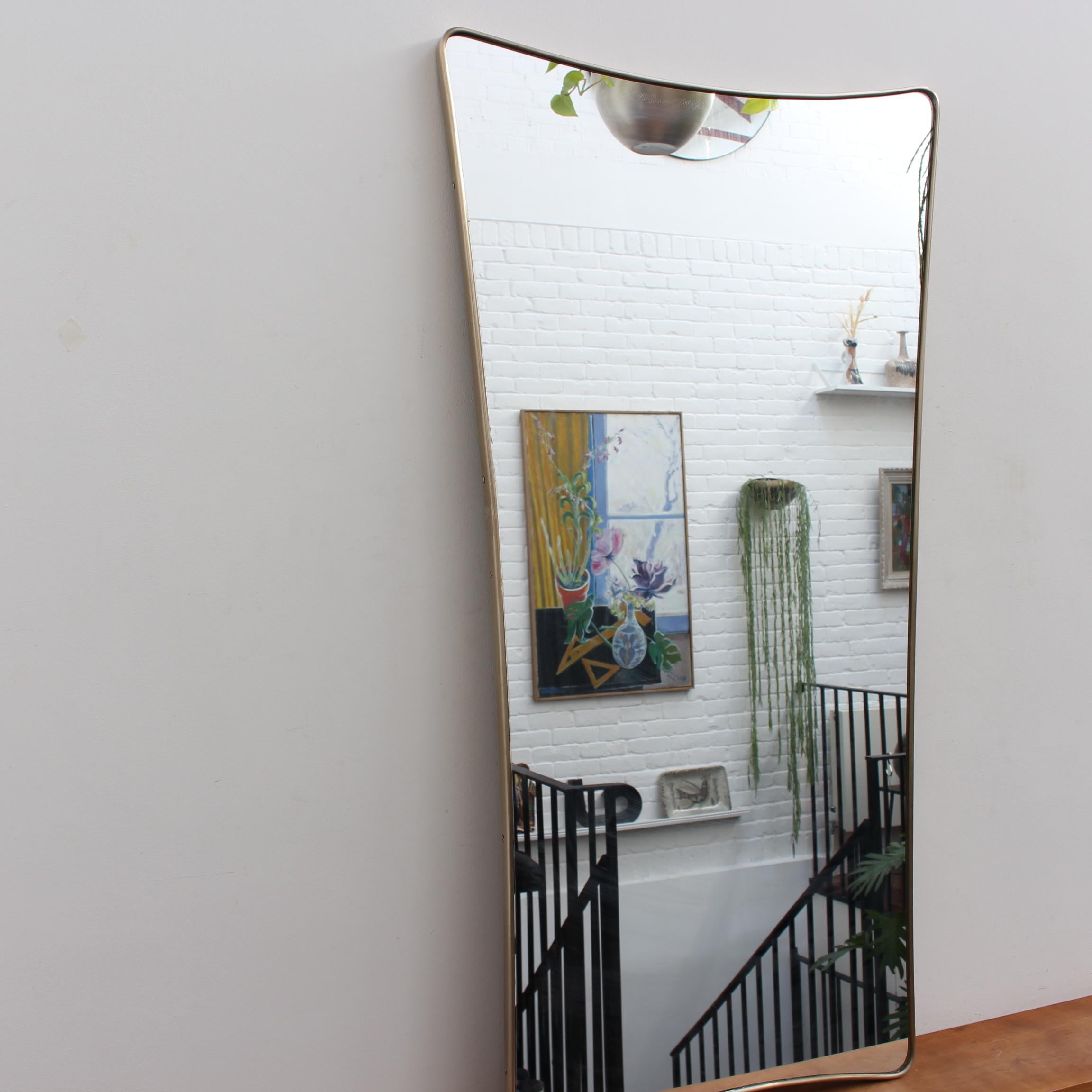 Midcentury Italian wall mirror with brass frame (circa 1950s). The large mirror is classically-shaped and distinctive in a Modern style. It is in very good overall condition. A beautiful, aged patina will appear on the brass frame although this one