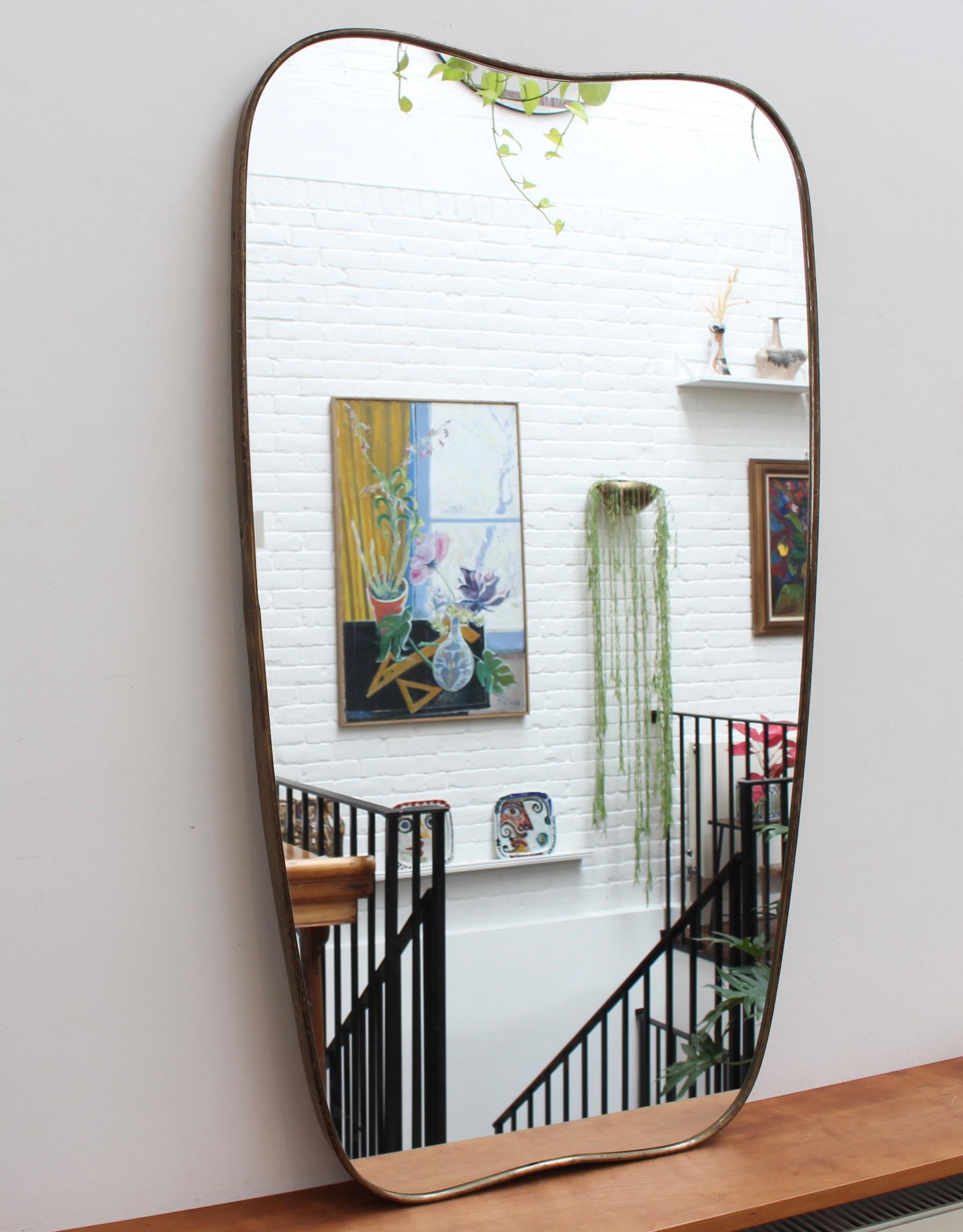 Mid-century Italian wall mirror with brass frame (circa 1950s). The mirror is classically-shaped and distinctive in a Modern style. It is in good overall condition. A beautiful patina develops on the brass frame - this one has not been polished but