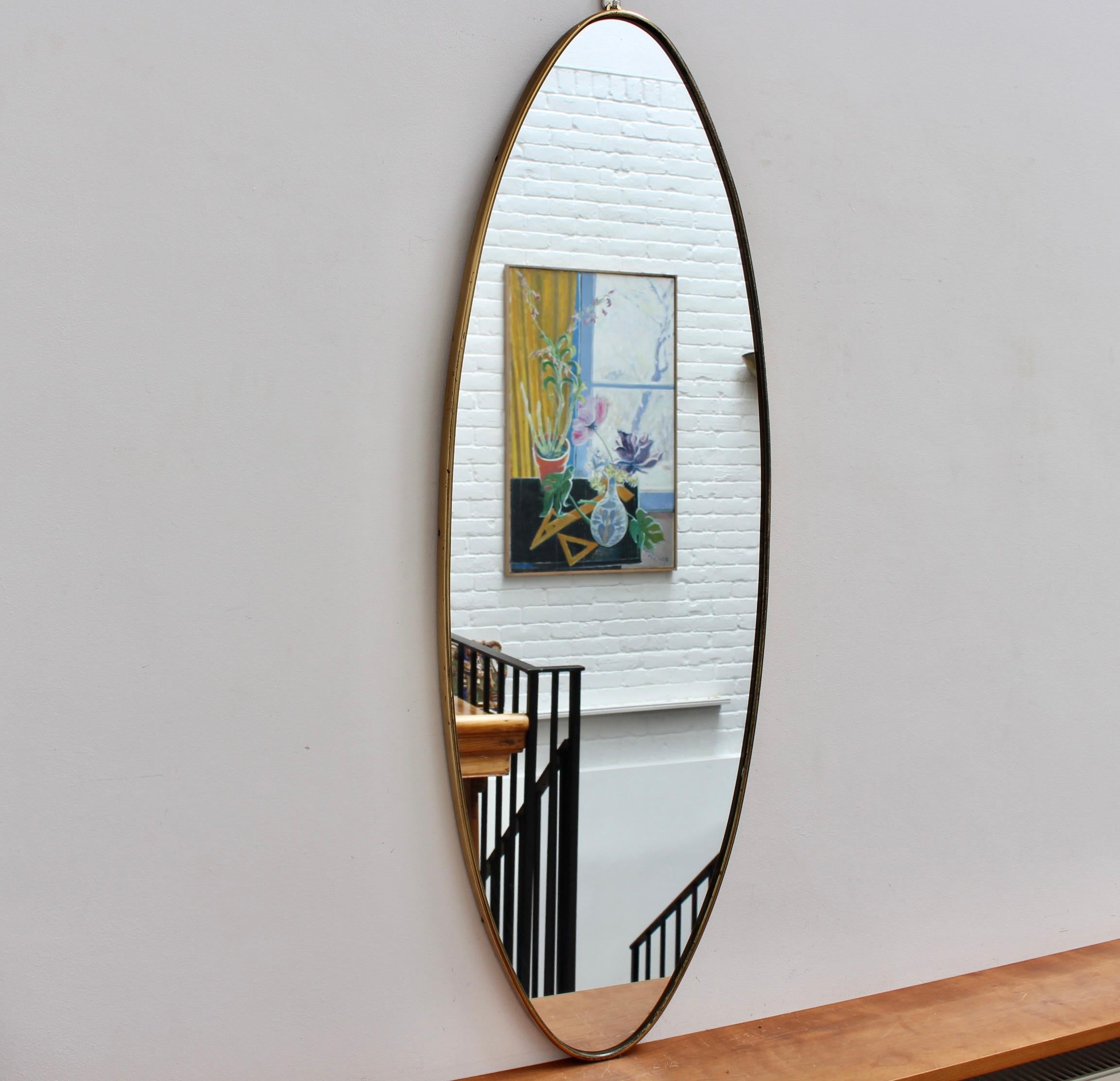 Mid-century Italian wall mirror with brass frame (circa 1960s). This sizeable mirror is oval-shaped and distinctive in a Modern style. It is in good overall condition. A beautiful patina has developed on the brass frame - the glass is in good