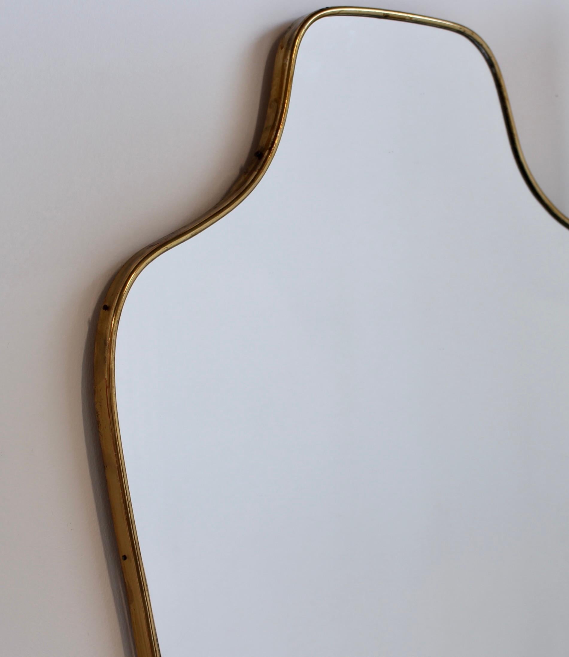Miroir mural italien du milieu du siècle avec cadre plaqué laiton (vers les années 1960). Le miroir est de forme classique et se distingue par son style moderne. Une patine de caractère se développe sur le cadre attestant de son ancienneté. Un