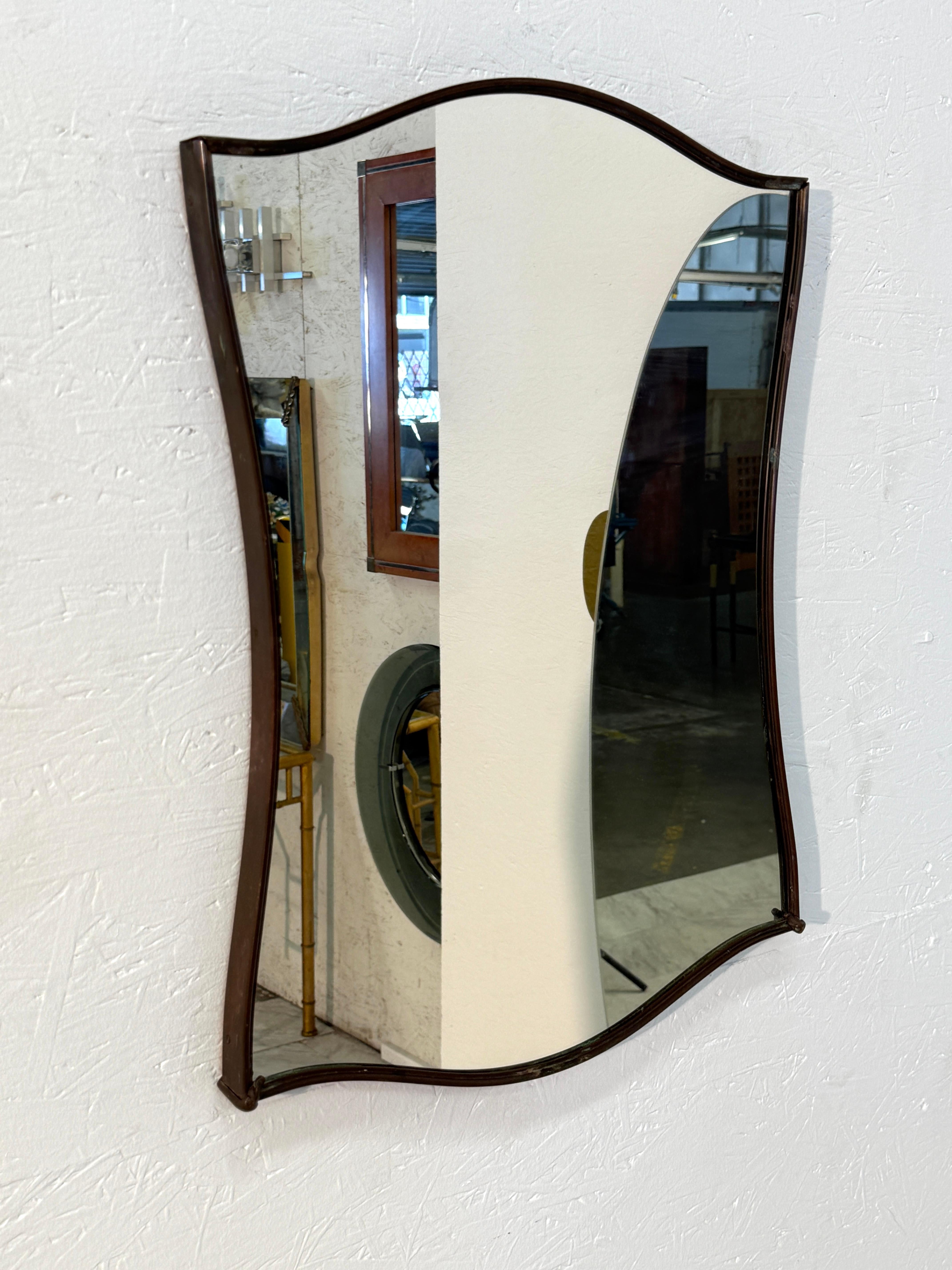 Dieser Spiegel zeichnet sich durch eine elegante, sanft geschwungene Silhouette mit einem dunkel bronzefarbenen Metallrahmen aus. Die subtile Wellenform des Glases verleiht ihm Raffinesse und macht es zu einem auffälligen Akzentstück sowohl für