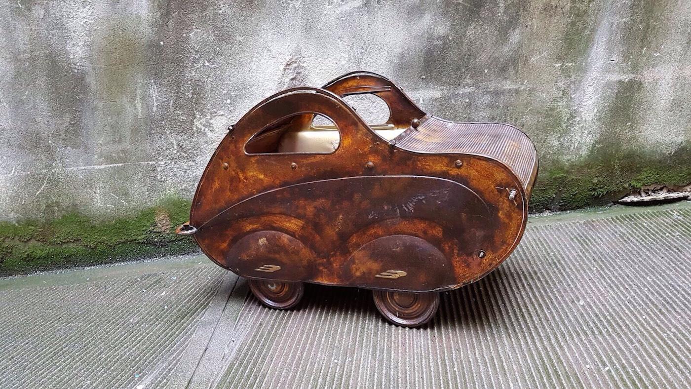 This amazing child's car-shaped pram was made in Italy by the Italian brand Giordani, this specif model was showed in their product's catalog of 1942.
It is made by brown painted iron and it is on sale along with its handle that fits on the back to