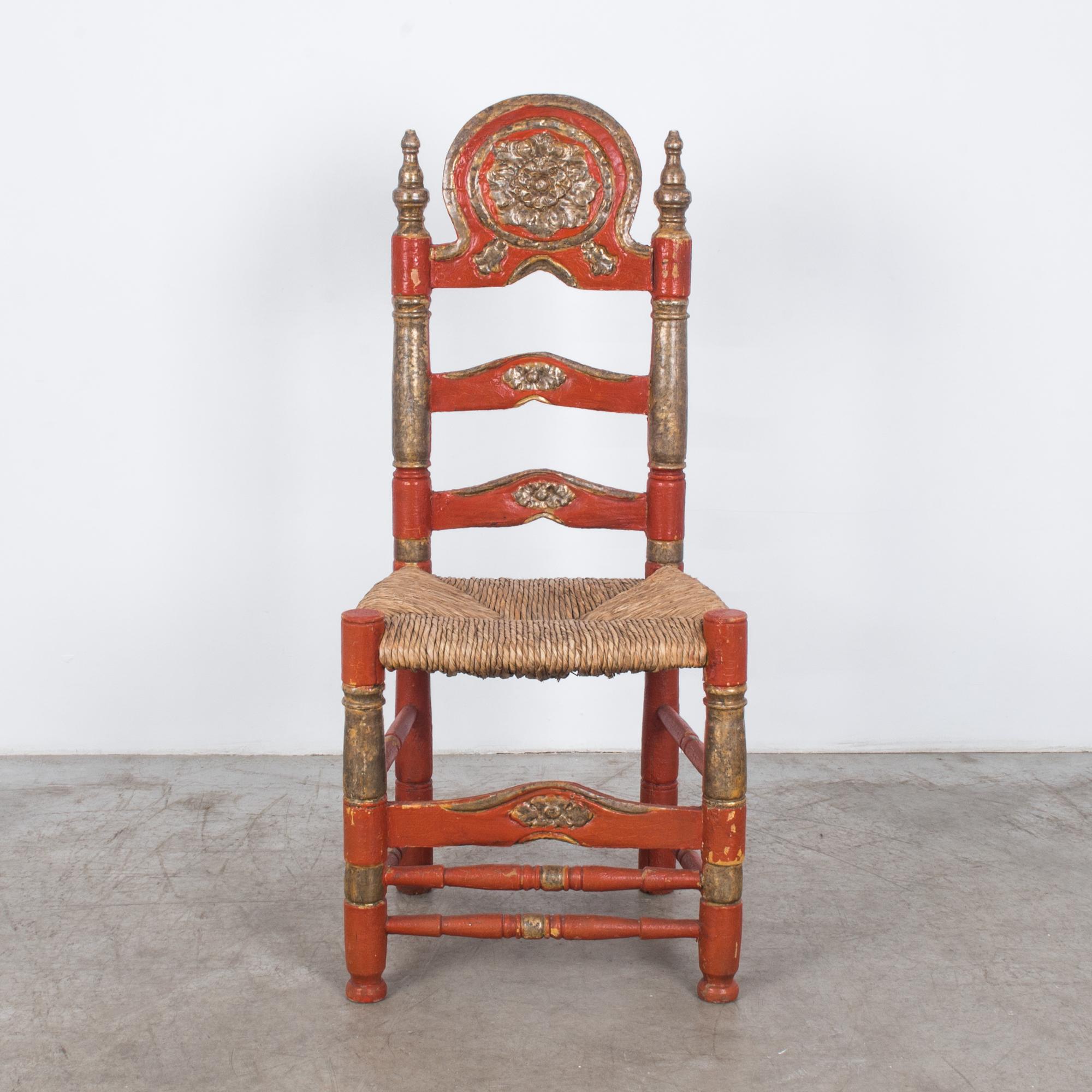 This stunning accent chair with a wicker seat was made in Italy, circa 1960. A rustic throne, large parts of the weathered wooden frame are painted terracotta red. The rear posts are topped with spires, which flank the impressive floral carving on