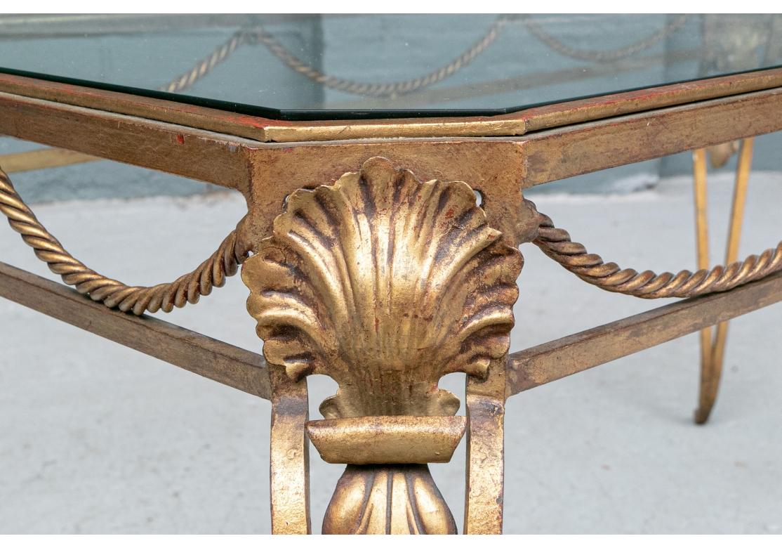Ein Cocktailtisch aus vergoldetem Eisen mit abgeschrägten Ecken, der Fries mit Seiltüchern, die sich anmutig durch die Ringe schlängeln, konforme Ecken mit Muschelmotiven und erhöht auf skulpturierten Haarnadelfüßen mit gerollten Füßen.
Abmessungen:
