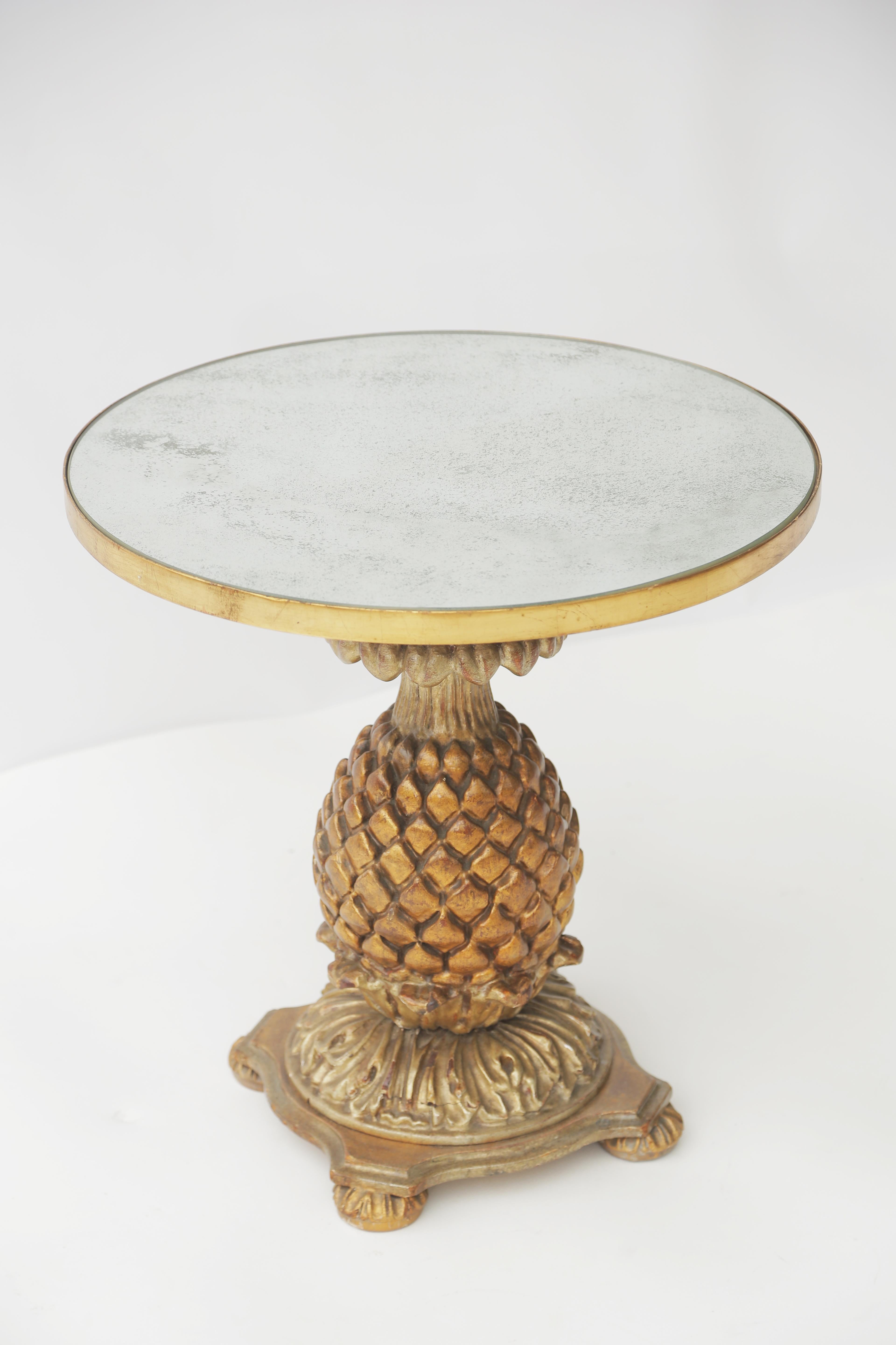 Side table, having a round top of aged mirrorplate with giltwood border, on base of wood, hand-carved in the form of a large, stylized pineapple; its body a darker stained wood with parcel gilt, on round, foliate foot, shaped plinth, and bun
