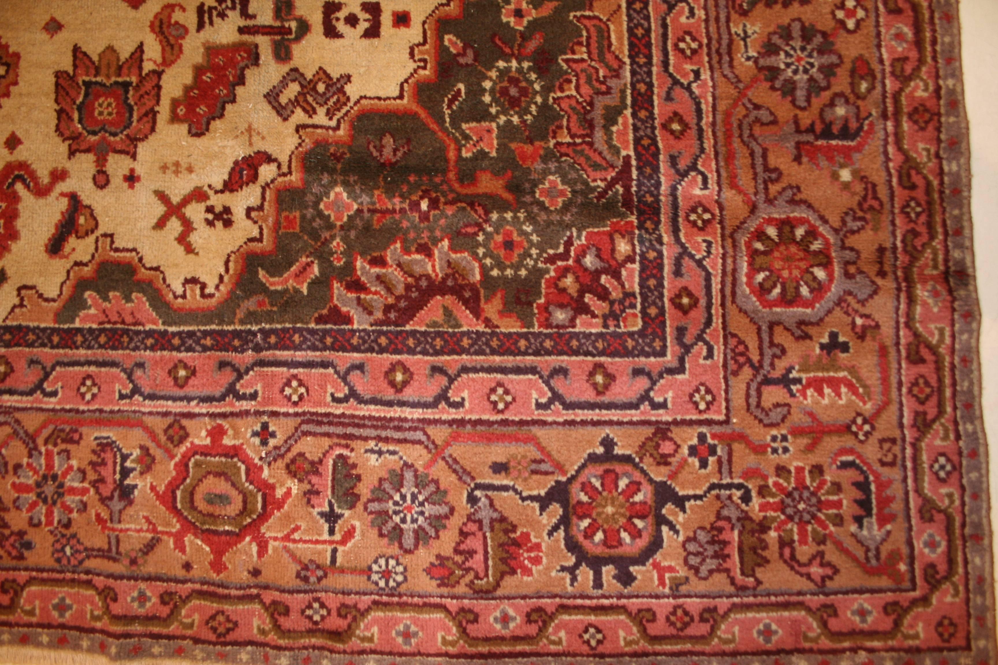 Dieser alte türkische Teppich zeigt ein persisches Muster, das aus einem zentralen Medaillon mit geviertelten Medaillon-Elementen in den Ecken besteht. Er zeichnet sich durch einen elfenbeinfarbenen Hintergrund und eine reiche Palette an dekorativen