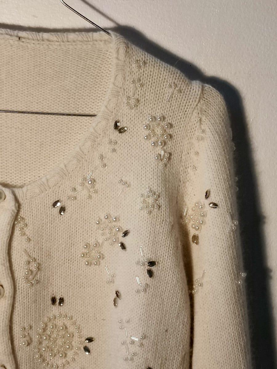 Exquisite, handverzierte Vintage-Strickjacke aus weicher elfenbeinfarbener Wolle aus den 1950er Jahren.
Dieses elegante Kleidungsstück ist reich verziert mit von Hand applizierten Perlen, Glasperlen und Pailletten, die auf der Vorderseite und den