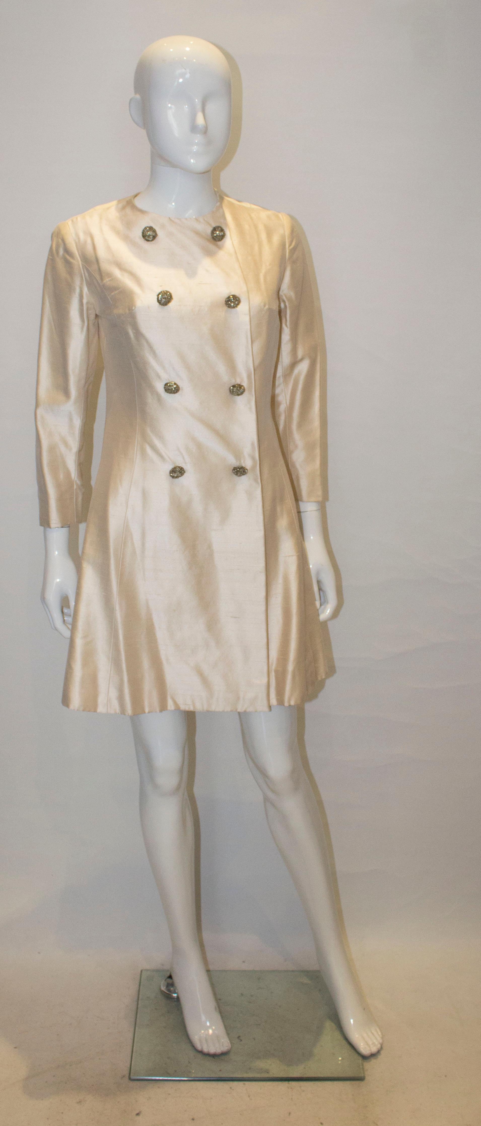 A chic vintage coat dress in raw silk. The dress has a round neckline, popper front fastenings with eight decorative buttons and is fully lined.
