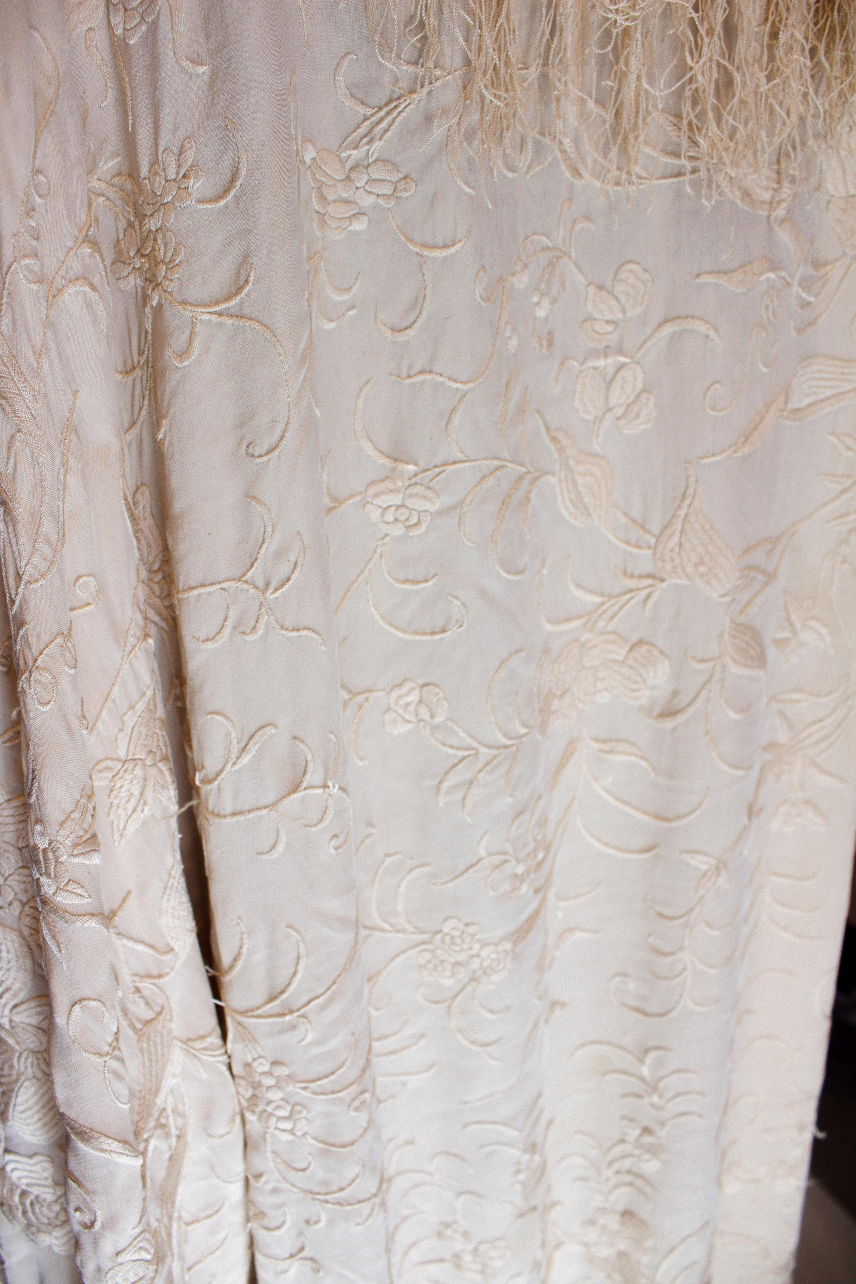 A stunning and large vintage piano shawl in ivory silk. The shawl is covered in floral embroidery and has fringing along the sides. Measurements 76'' x 76''