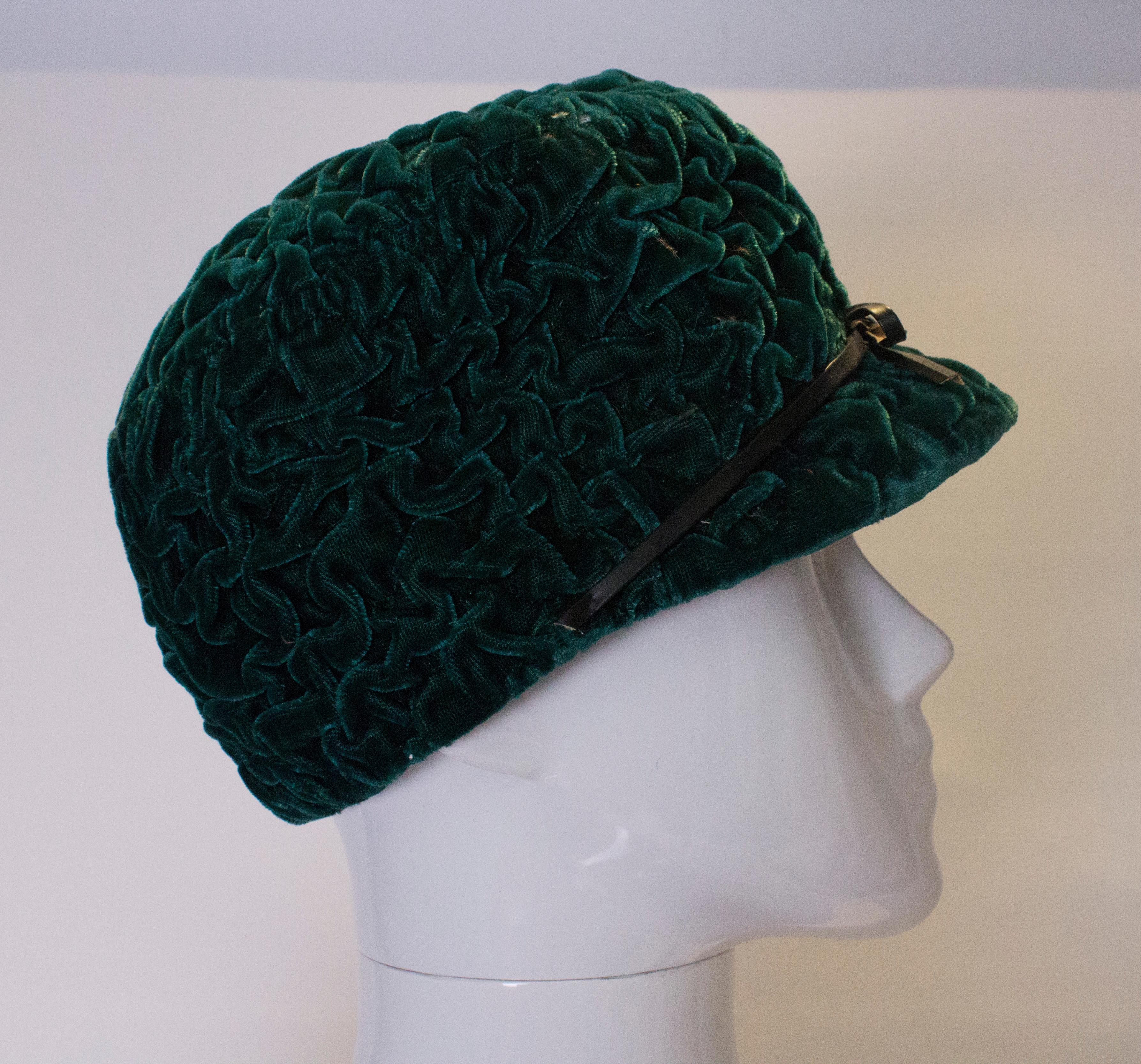 A fund green velvet hat by Jaccoll. The velvet has an interesting texture and is decorated with a black leather ribbon. 