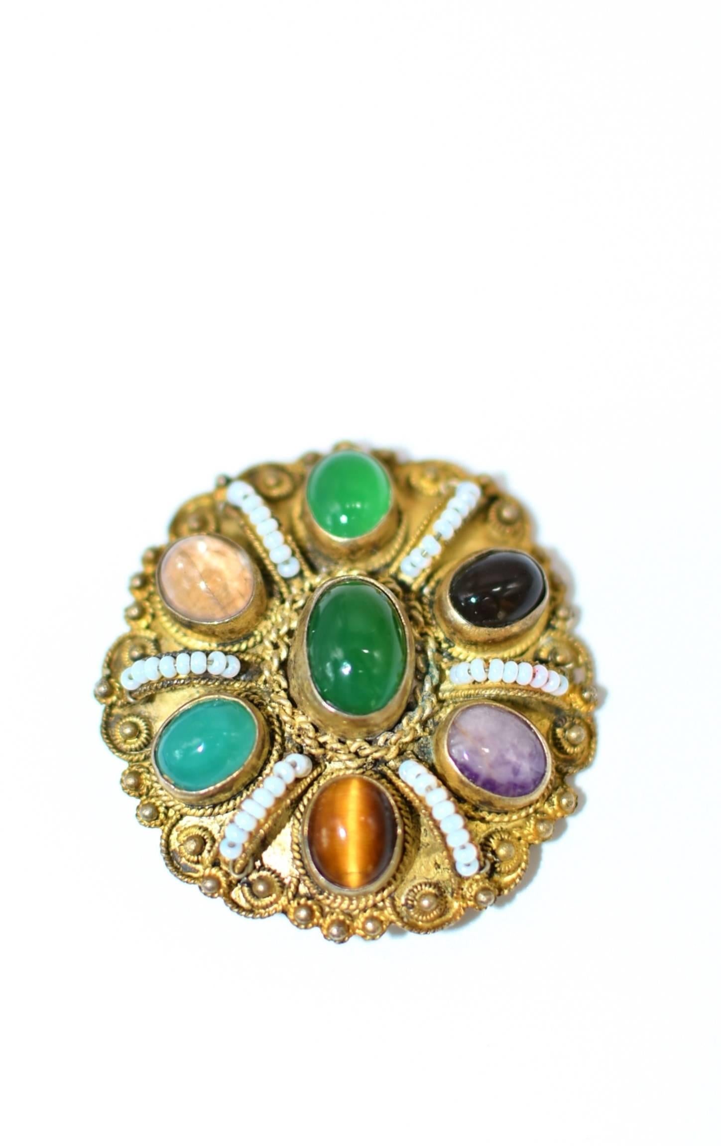 A stunning vintage piece. The brooch/pendant is encrusted with seven beautiful gemstones, including jade, crystal, tiger's eye, aventurine, smoky quartz, serpentine and amethyst. It is trimmed with delicate fancy scroll works. Six lines of white