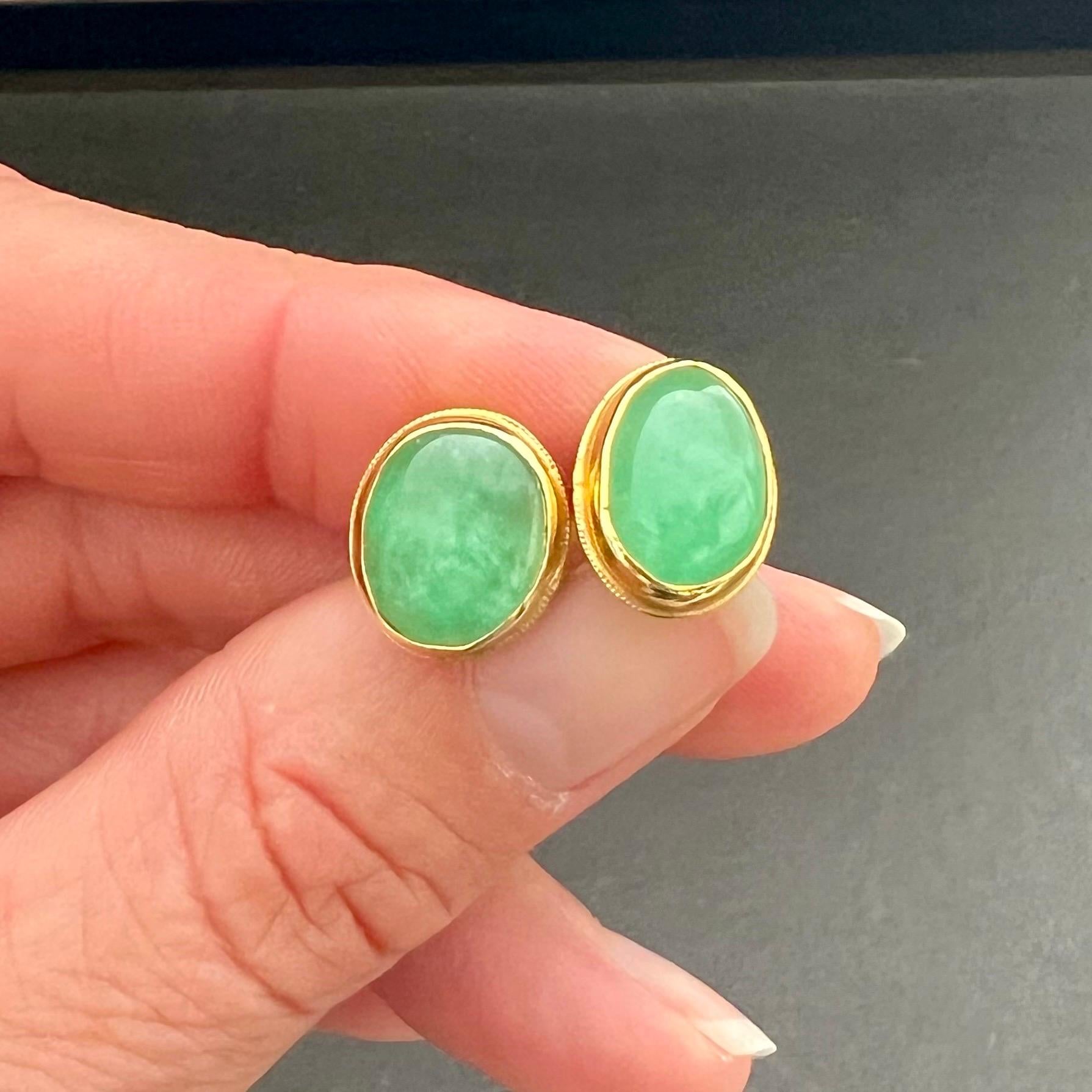 A lovely vintage pair of green jadeite jade earrings. The natural jadeite jade is bezel set in an 18 karat yellow gold frame. The earrings are designed with an oval cabochon cut green translucent jade stone. The jade has an immense vivid green color