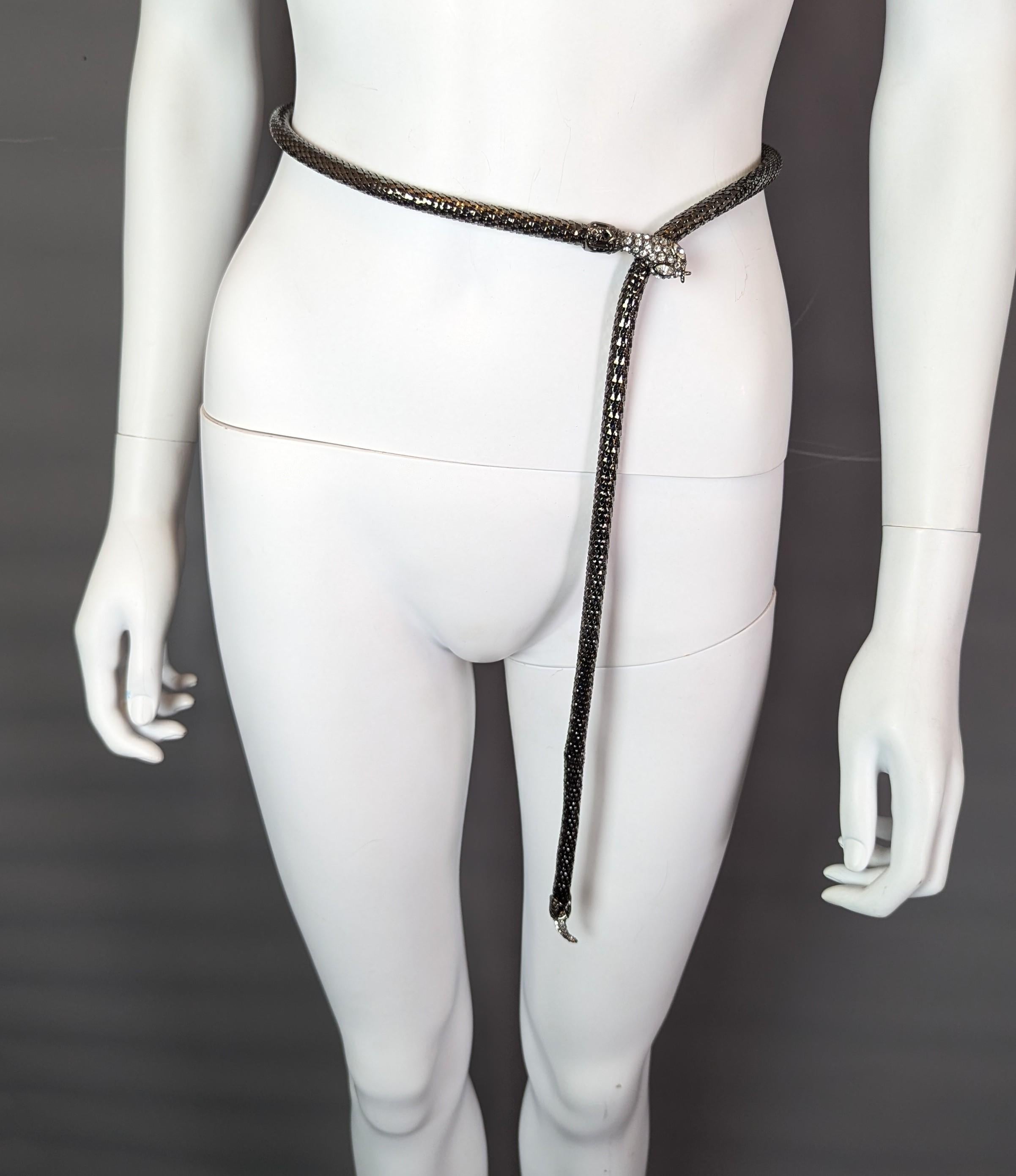 Un fantástico cinturón vintage Jaeger con diseño de serpiente.

Fabricado en metal gris plomo con un núcleo flexible, el cuerpo se ha diseñado para imitar las escamas de una serpiente y el cinturón se abrocha con un clip de presión.

La cabeza tiene