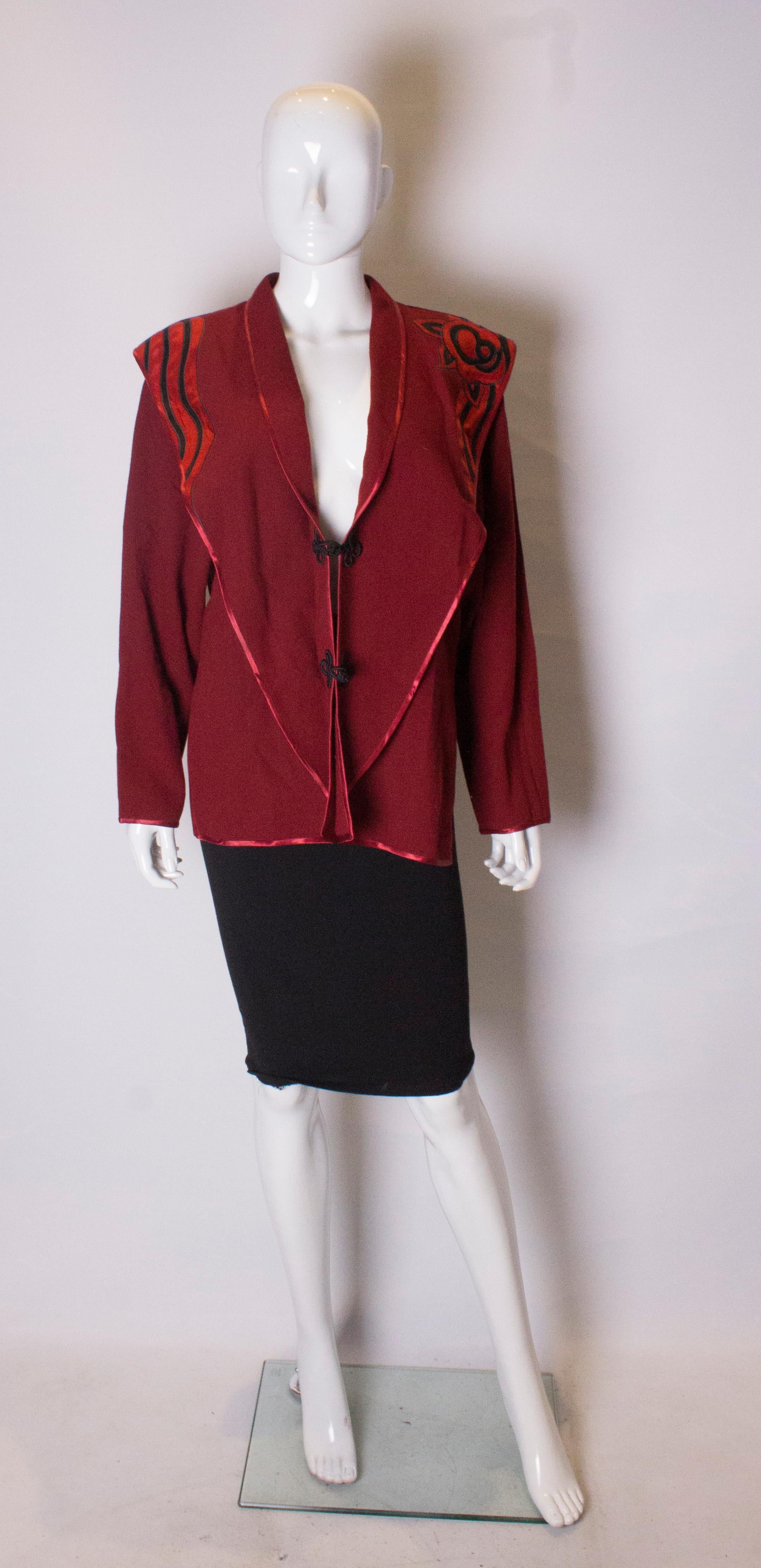 A great jacket in wool crepe by Janice Wainwright.  The jacket is edged  in ribbon, and has a black and red decorative detail. It has toggle fastening and a 9'' slit on either side.