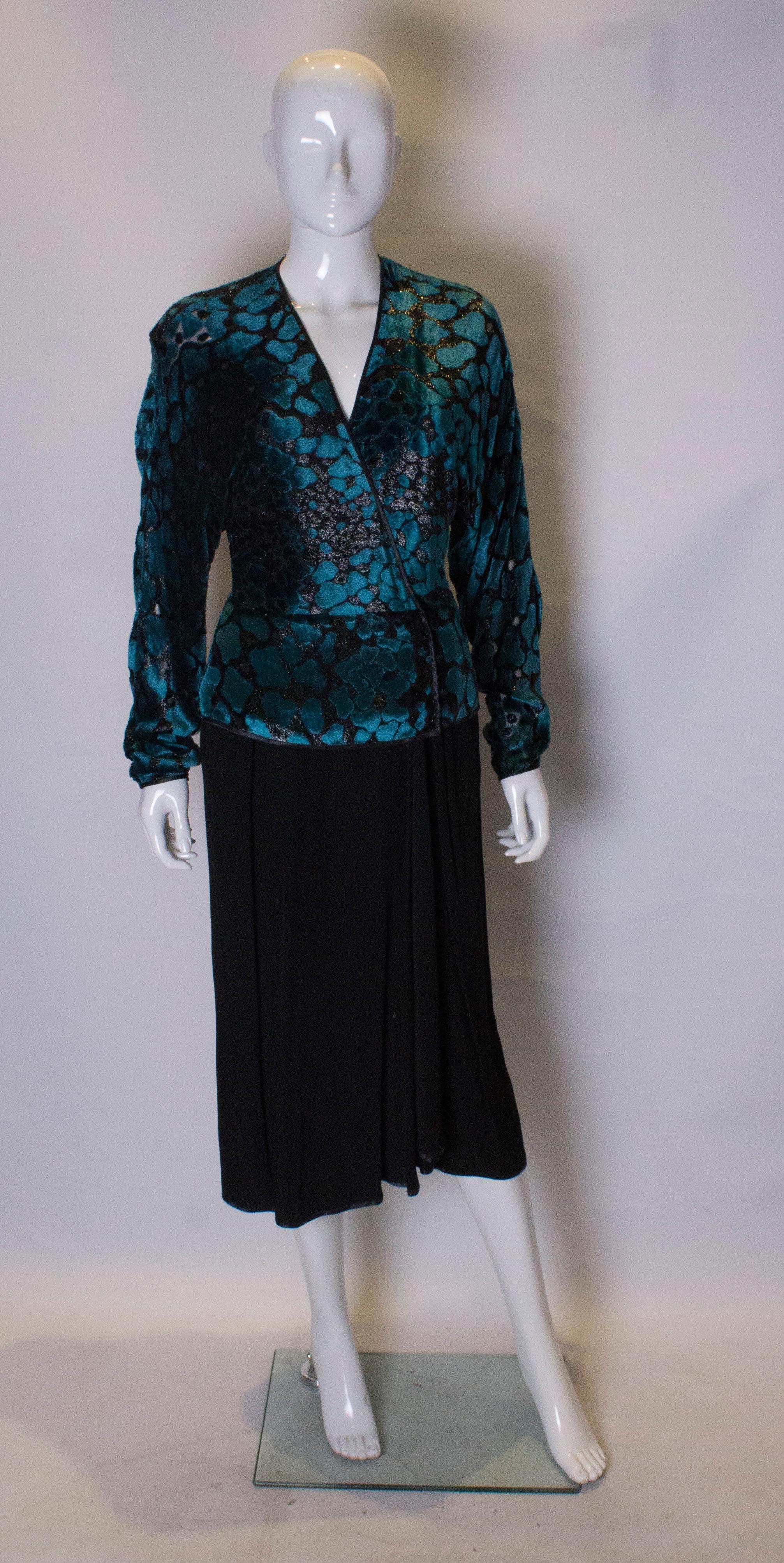 A chic and easy to wear cocktail dress by  UK designer Janice Wainwright.The dress has a turquoise and black devoree velvet top with the a black skirt. It has a V neckline, with a front button opening, and folds over with a slight peplum. The