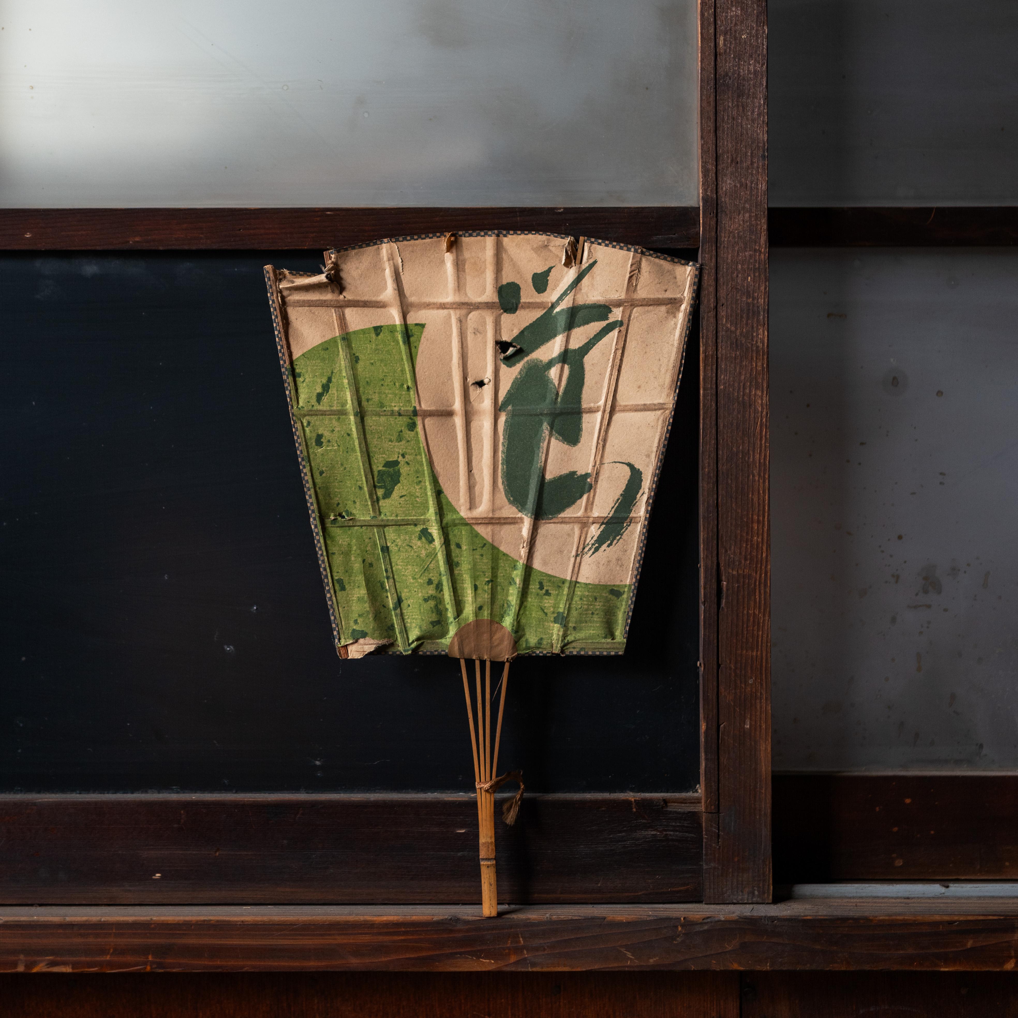 Un rare exemple d'éventail traditionnel japonais uchiwa, présentant une composition graphique audacieuse de couleur verte et crème. La surface plane et rigide, fabriquée à partir de rayons de bambou et de papier, conserve un caractère riche et des