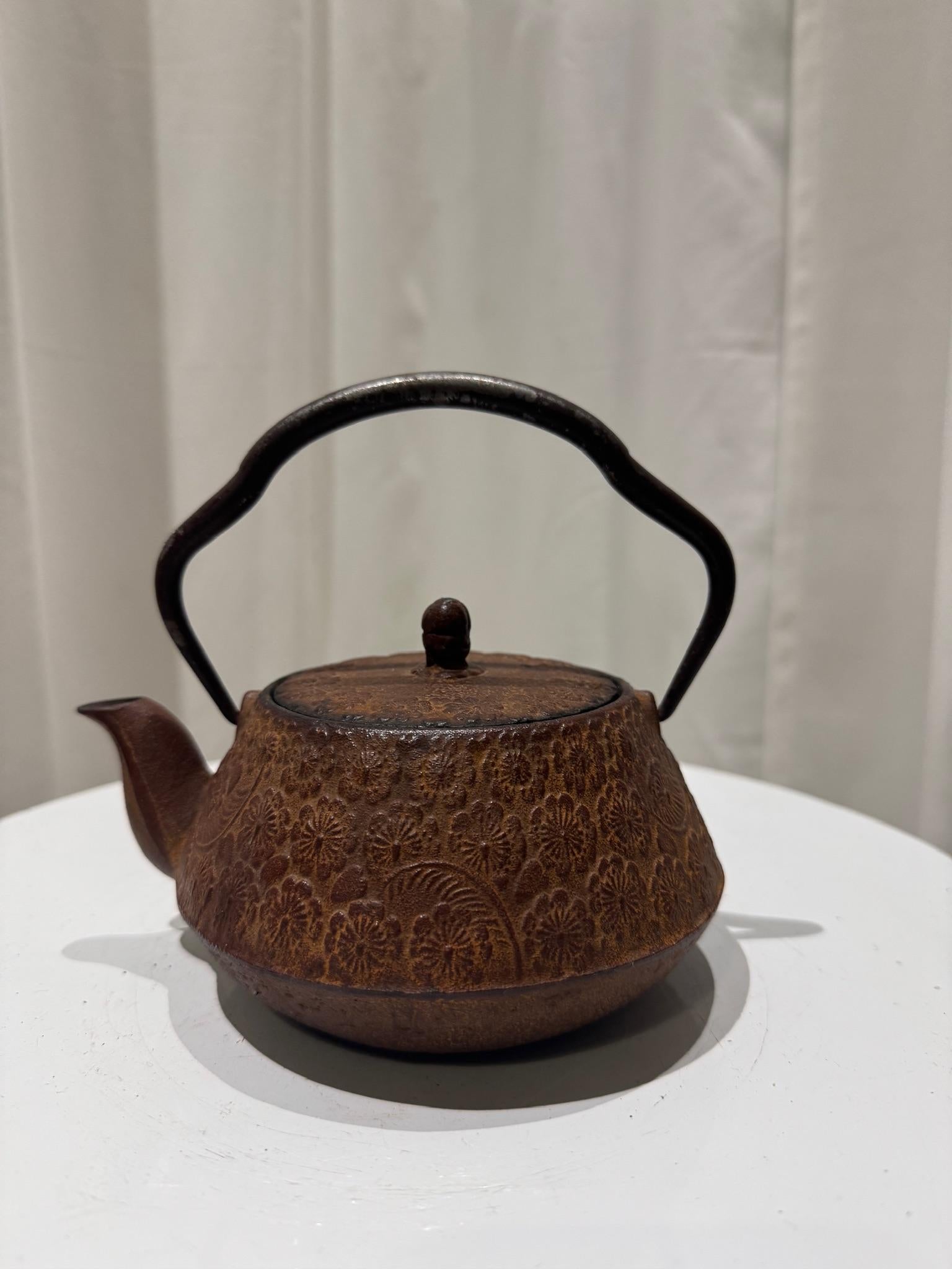 This exquisite vintage Japanese cast iron Tetsubin teapot showcases a beautifully embossed floral relief pattern, embodying the elegance of traditional craftsmanship. With its gracefully curved iron handle and richly textured surface, this teapot is