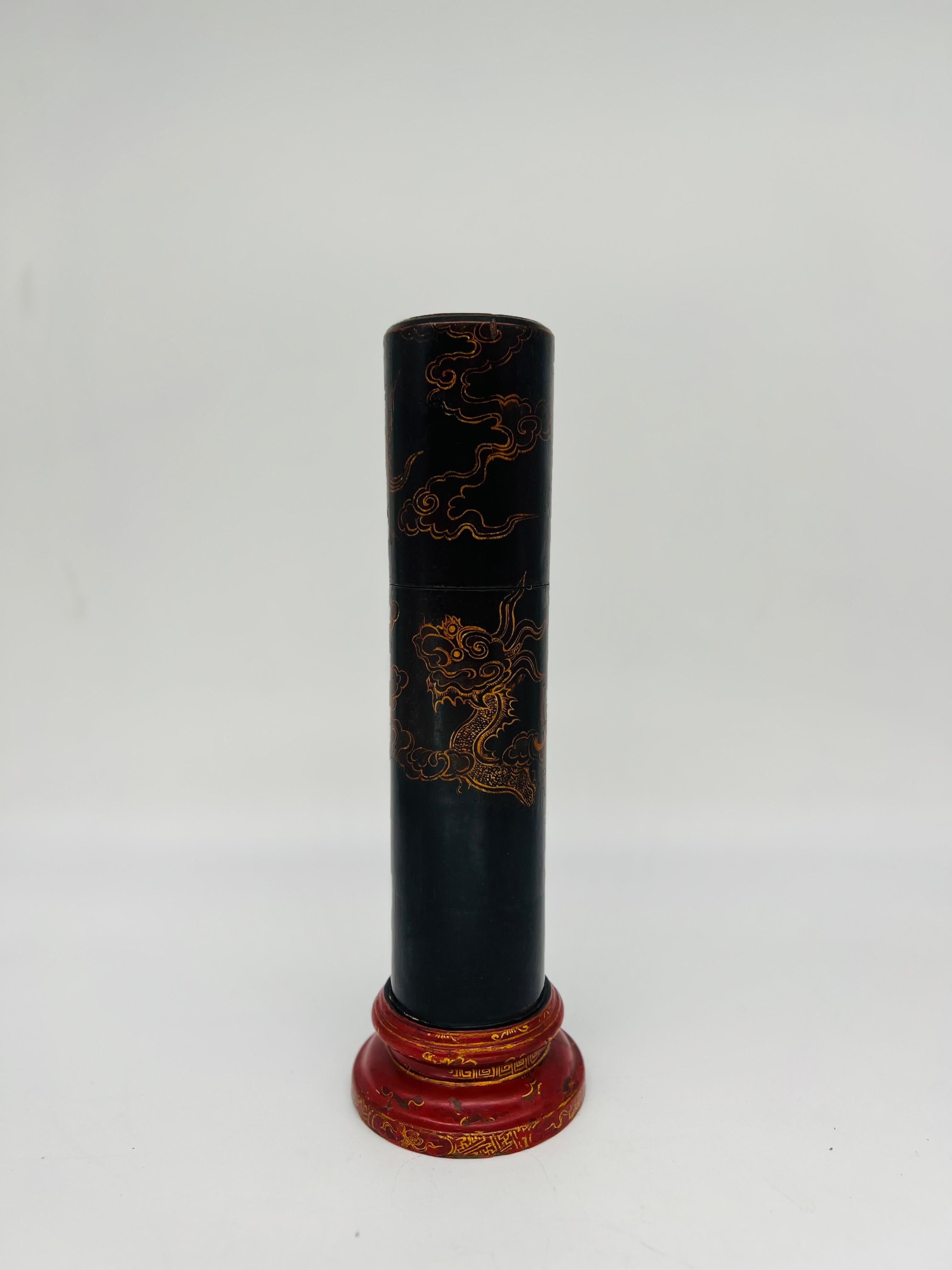 A fine vintage match-strike box. The box, likely of Japanese origin features a cylindrical body heavily decorated with a black lacquer paint and embellished with gilt a clawed dragon. The base is a stepped red lacquer with geometric pattern and the