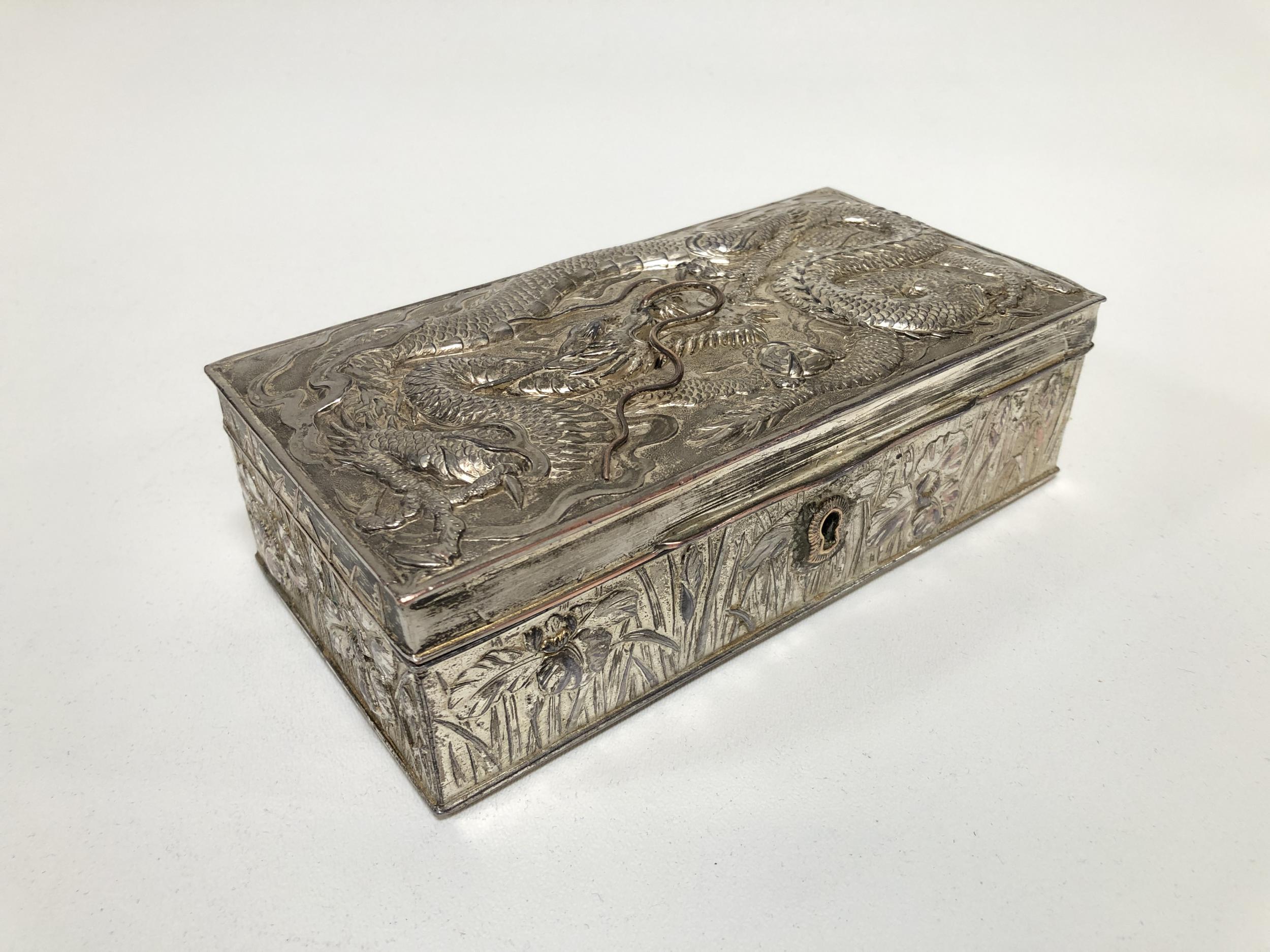 This beautiful ornately repousse silver-plated keepsake or jewelry box features a detailed dragon on top and grass-like designs on the sides. The interior is mahogany wood. This piece is projected to be from Japan in the 1920's.

This box features