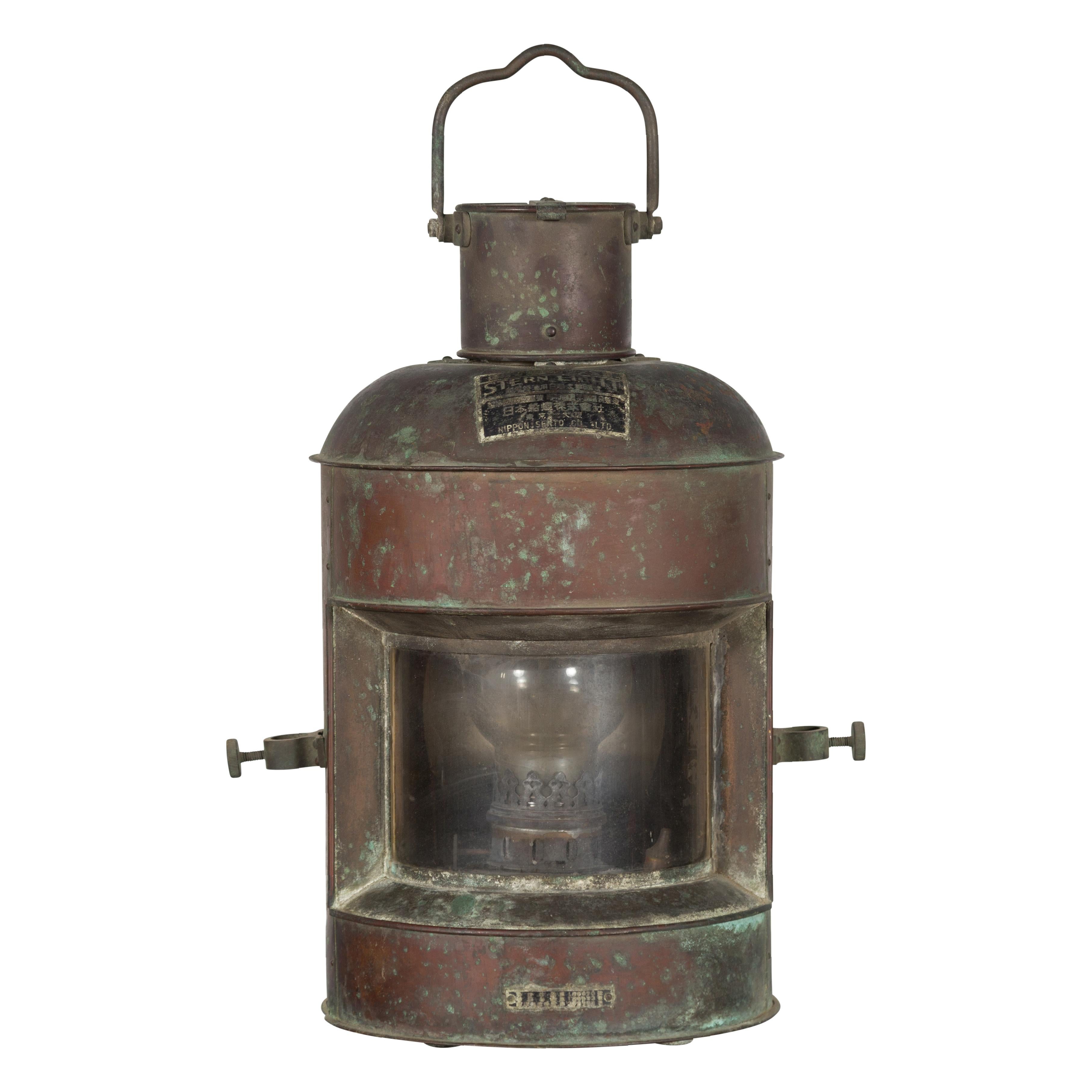 A Japanese metal ship's navigation stern light from the mid 20th century, made by Nippon Sento Co, ltd, with oxidized patina. Created in Japan during the mid 20th century, this stern light showcases a partially cylindrical shape topped by a hoisting