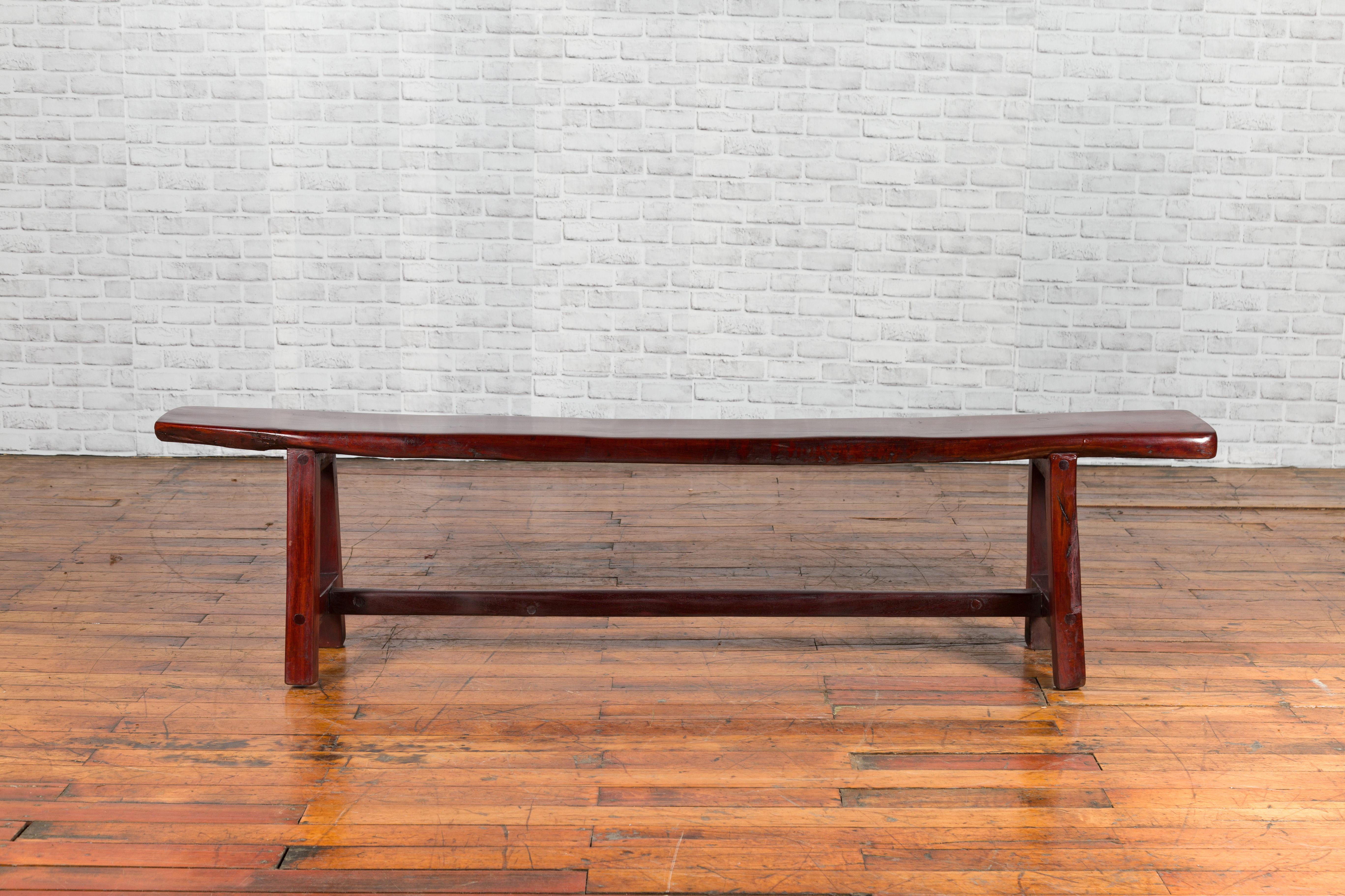 A vintage Javanese A-frame bench from the mid-20th century, with dark patina. Created in Indonesia during the midcentury period, this rustic bench features a long rectangular seat resting on an A-frame base with simple cross stretcher. Placed