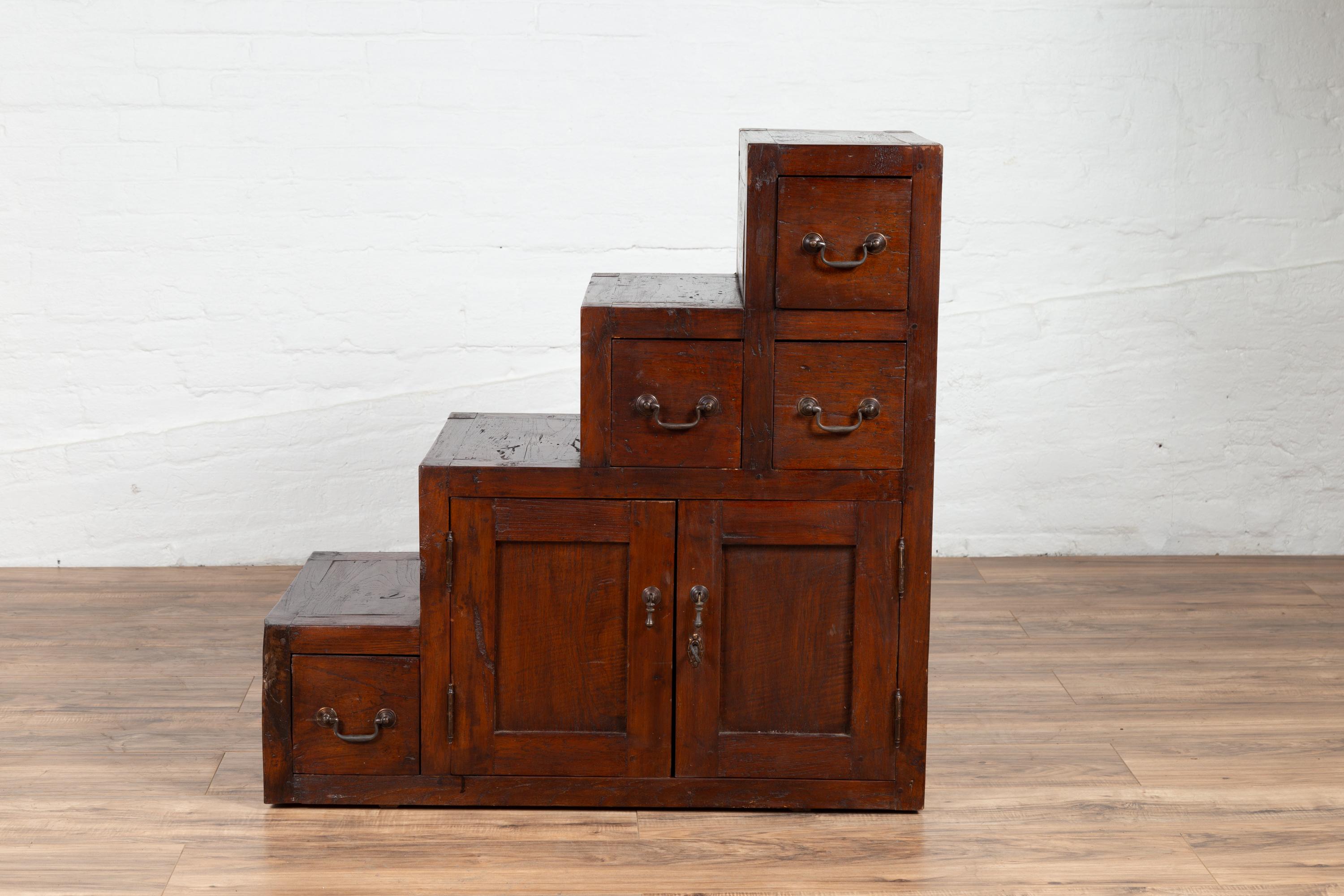 A vintage Javanese staircase tansu in Japanese style from the mid 20th century, with four drawers and double-door cabinet. Inspired by a 19th century Japanese design, this staircase tansu features a convenient stepped storage unit presenting a warm