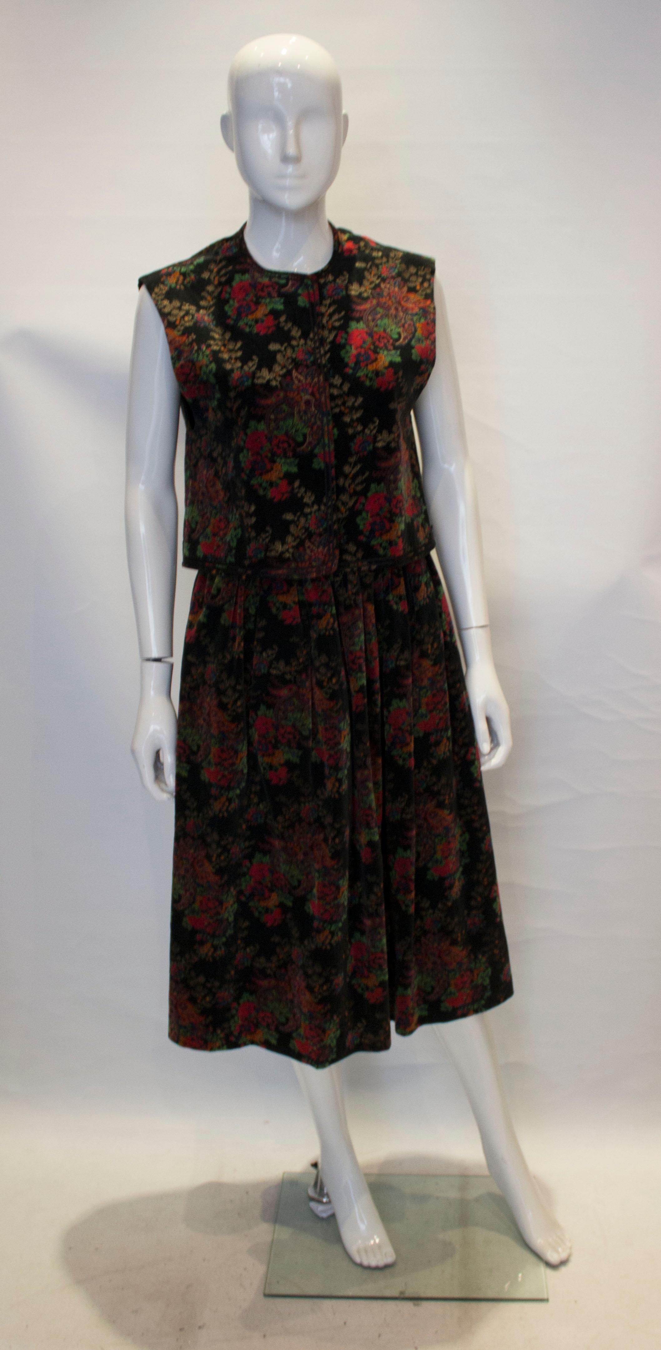 A vintage outfit by Jaeger,. In a  back velvet with floral print, the waistcoat has a round collar and two rows of braid. The skirt has gathering at the waist , two pockets and is fully lined.

Measurements: waistcoat bust 37'', length 19'', skirt