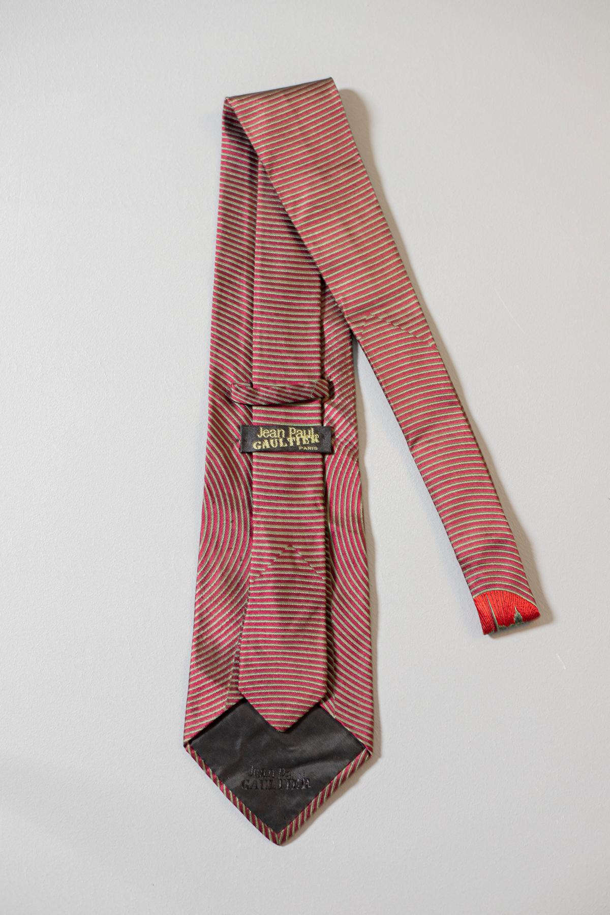 Unique and original, this all-silk tie was designed by Jean Paul Gaultier. It is in all-silk and it displays a golden heart with a sword on a golden and red background. This tie is perfect if you want to stand out from the crowd.