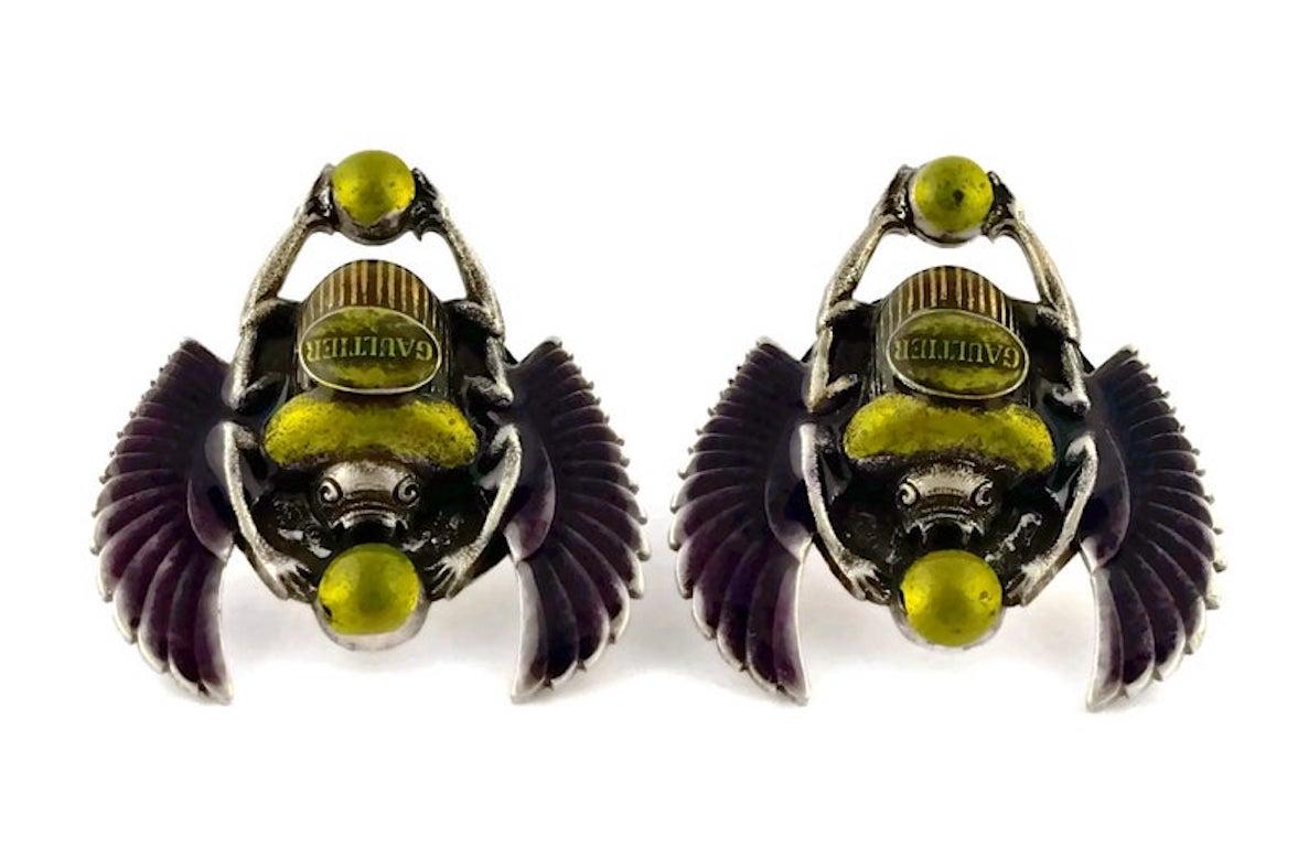 Vintage JEAN PAUL GAULTIER Enameled Scarab Egyptian Earrings

Measurements:
Height: 1 5/8 inches
Width: 1 4/8 inches

Features:
- 100% Authentic JEAN PAUL GAULTIER.
- Enameled scarab beetle in olive green and violet.
- GAULTIER logo at the centre.
-