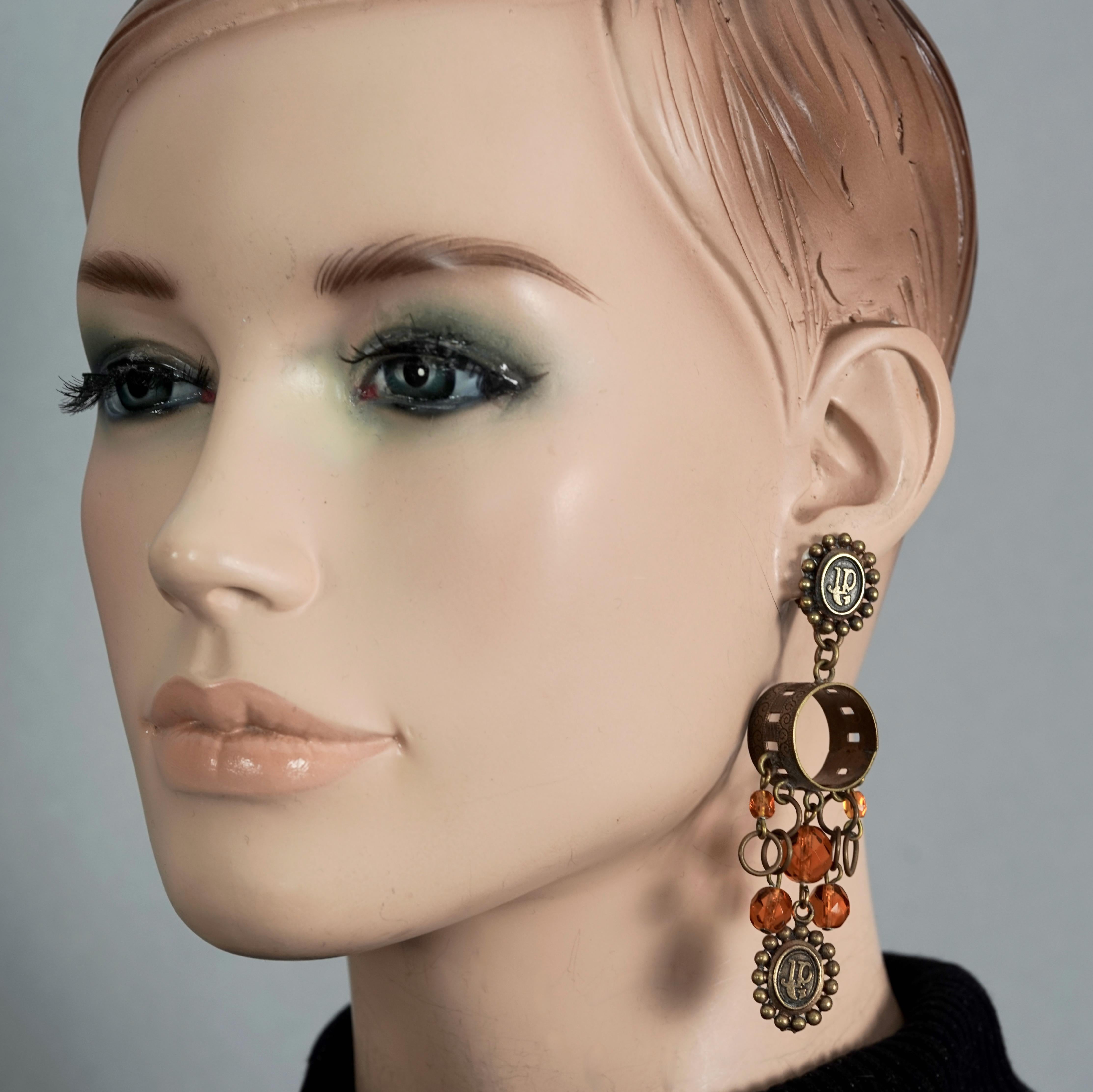 Vintage JEAN PAUL GAULTIER Logo Amber Beads Hoop Dangling Earrings

Measurements:
Height: 3.74 inches (9.5 cm)
Width: 0.38 inch (0.98 cm)

Features:
- 100% Authentic JEAN PAUL GAULTIER.
- Dangling earrings with embossed JPG logo medallions, hoop and