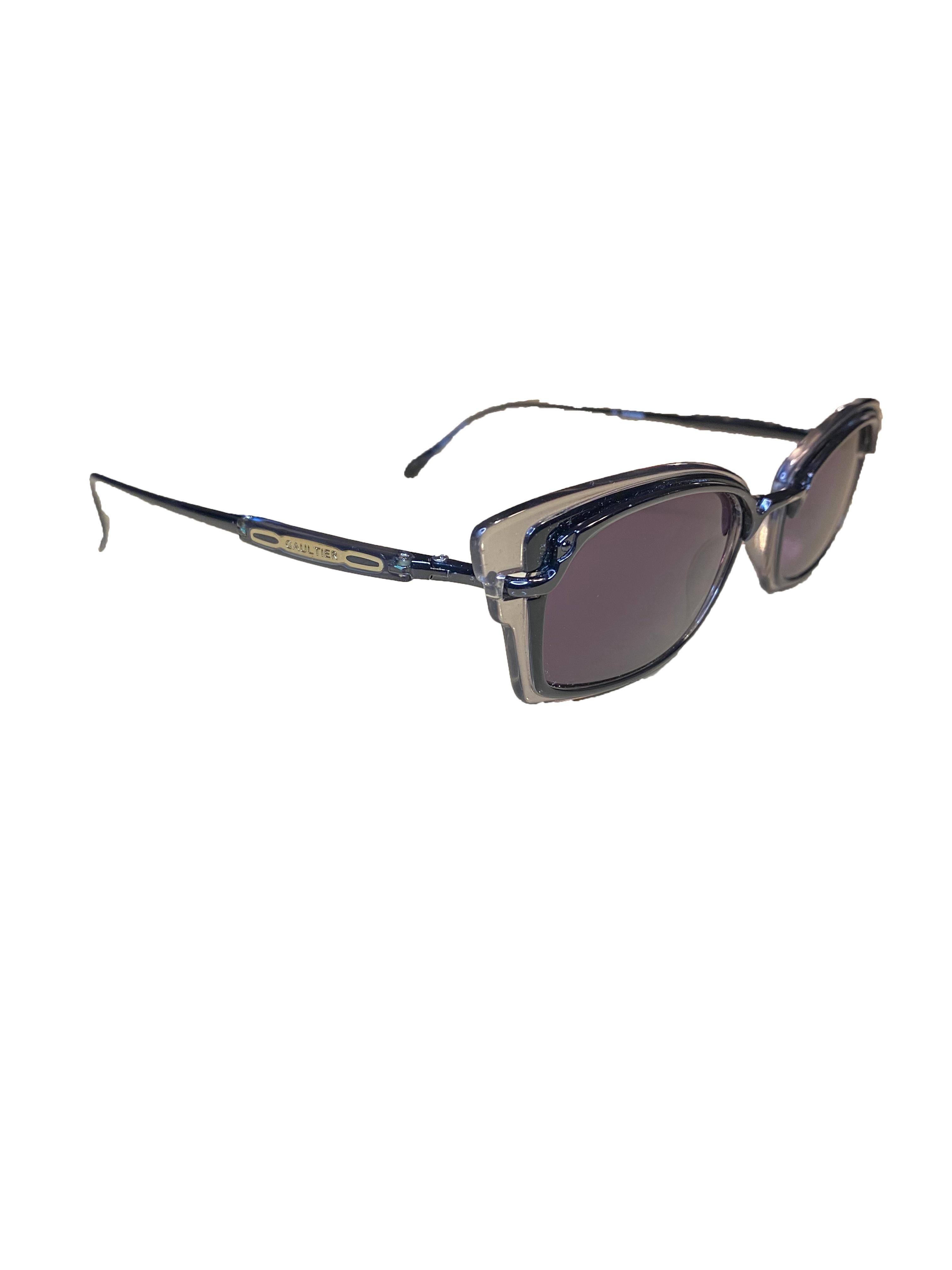 Vintage sunglasses by Jean Paul Gaultier. Black acetate inner frame and clear acetate surround in cats eye shape with dark tint on the lenses. Black narrow metal legs with acetate badge at both temples, carrying metal logo and 