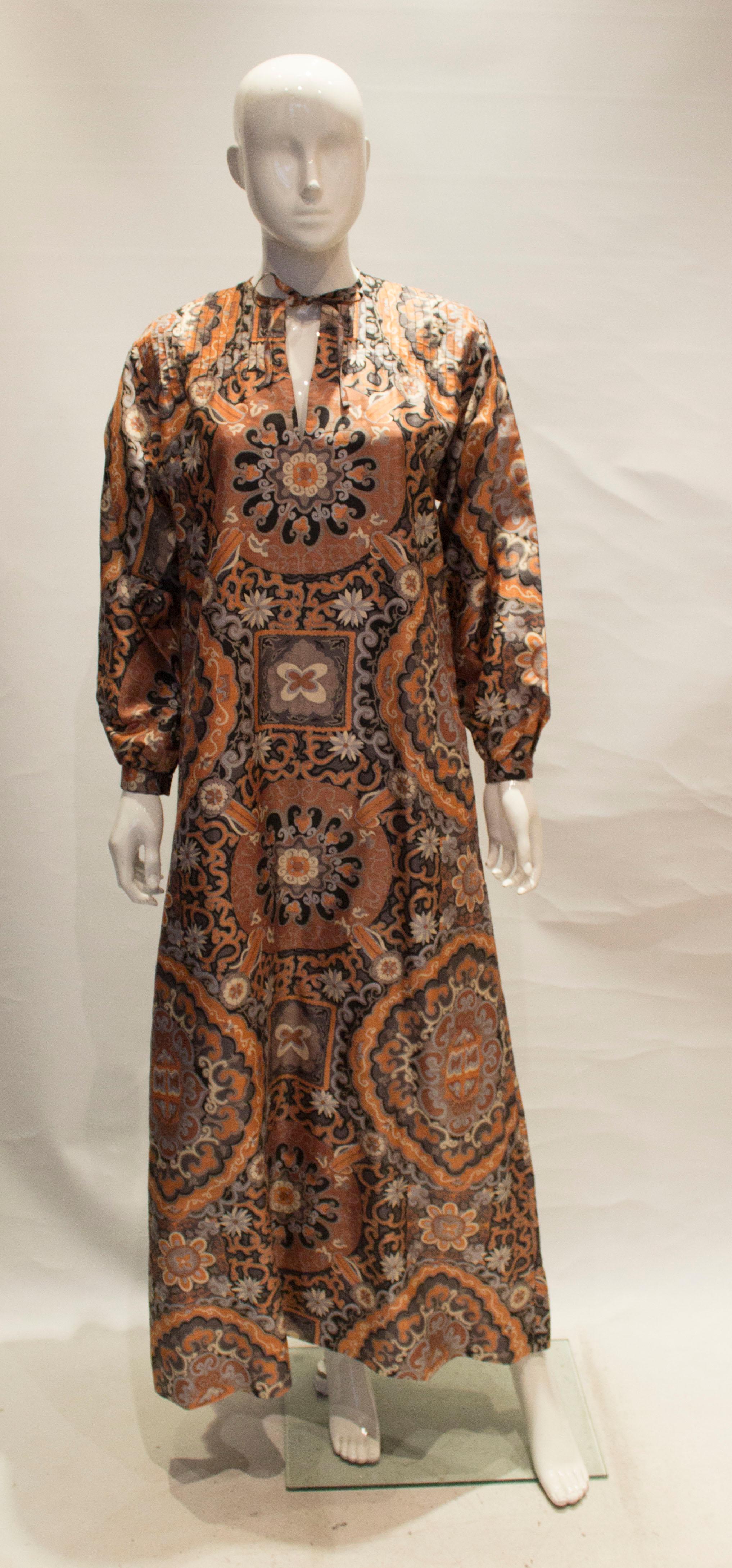 A great silk kaftan ideal for holiday and cruise wear. The kaftan is in a wonderful print of grey , orange and ivory.  It has pintucks on the shoulders and pockets on either side . 
It is best worn loose and will fit bust up to 40'', length 53''