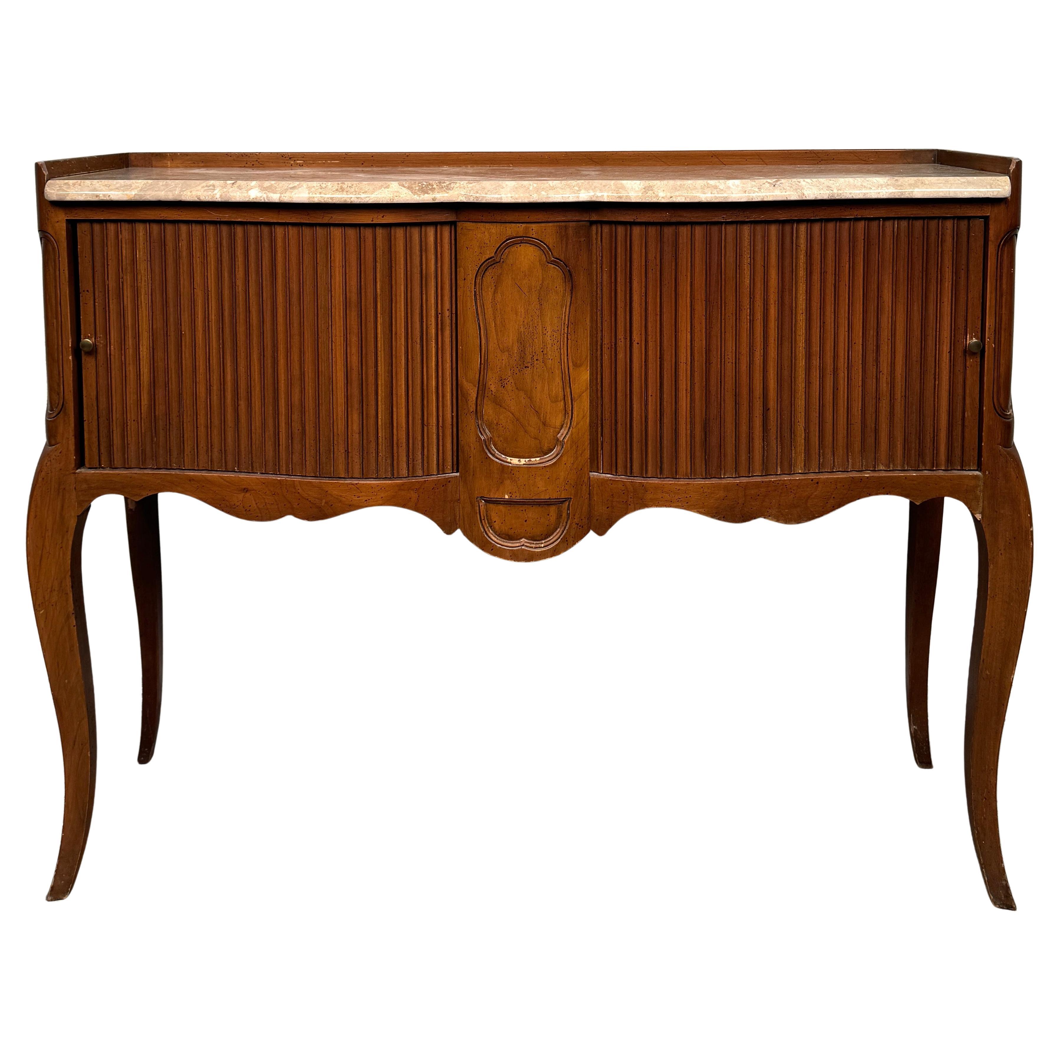 Refined, regal, and rich in detail, this vintage console table by John Widdicomb is a masterclass in craftsmanship and timeless elegance. Blending French neoclassical styling with American luxury, this piece features a sumptuous marble top set above