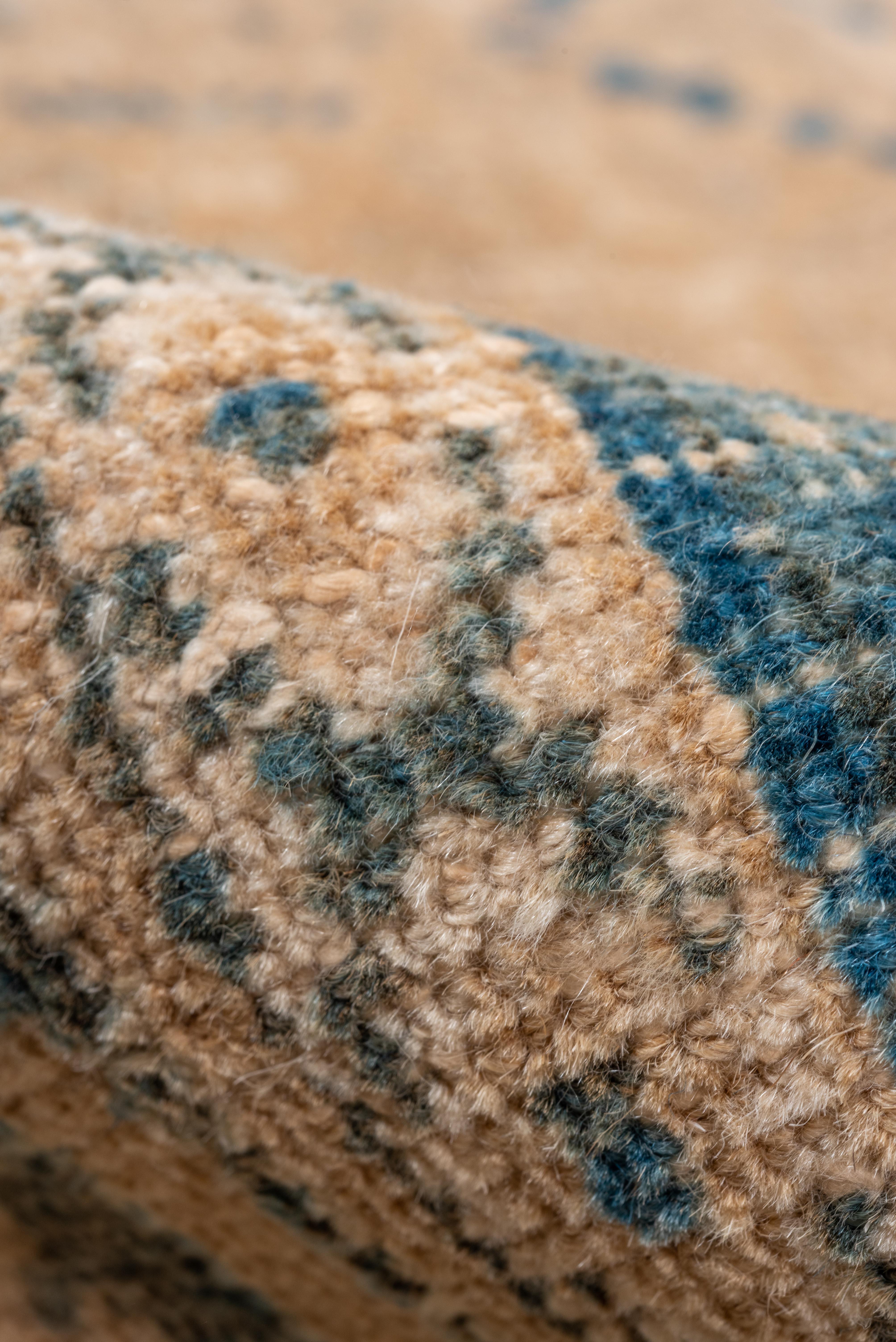 Ce tapis Joshegan vintage présente un motif traditionnel de treillis en losange, rendu de manière complexe dans des tons de camel, de sable et de bleu denim. Le champ est rempli de rangées de losanges imbriqués contenant des fleurs stylisées et des